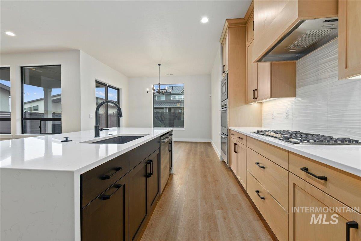 Kitchen featuring premium range hood, light stone counters, light wood finished floors, light brown cabinets, and hanging light fixtures