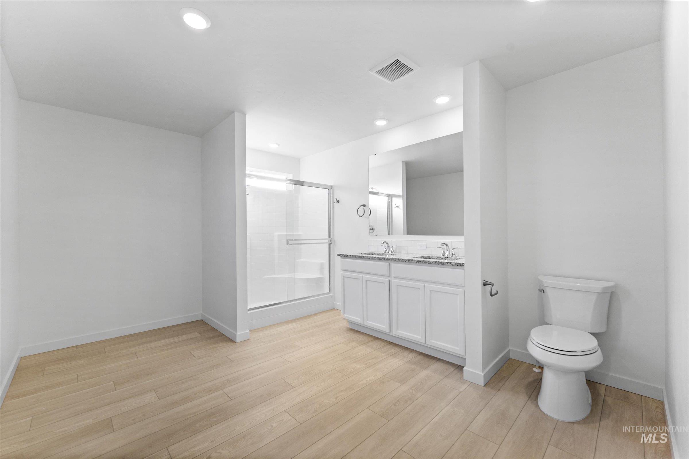 Bathroom with double vanity, a shower stall, light wood-type flooring, and recessed lighting