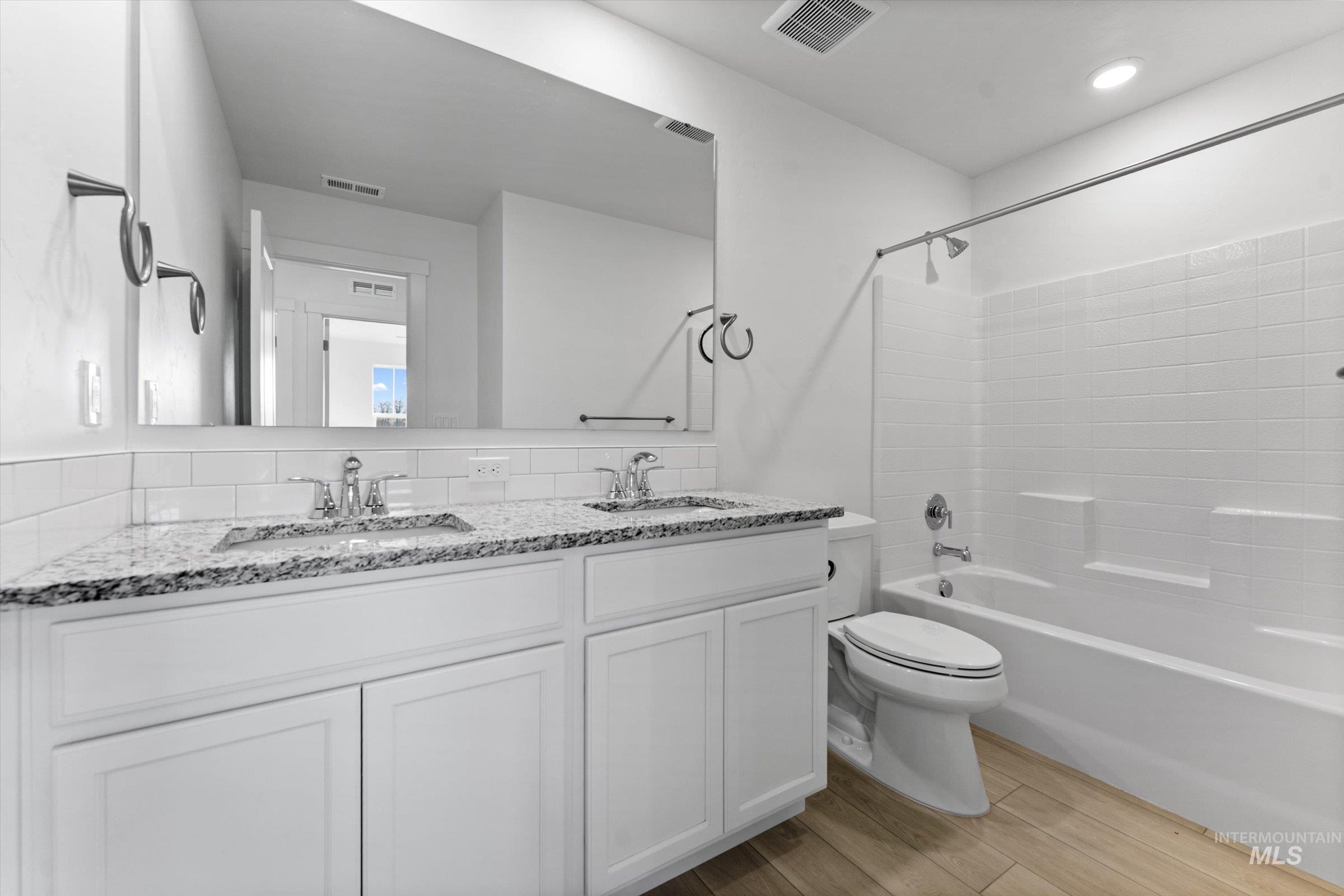 Bathroom featuring double vanity,  shower combination, and light wood finished floors
