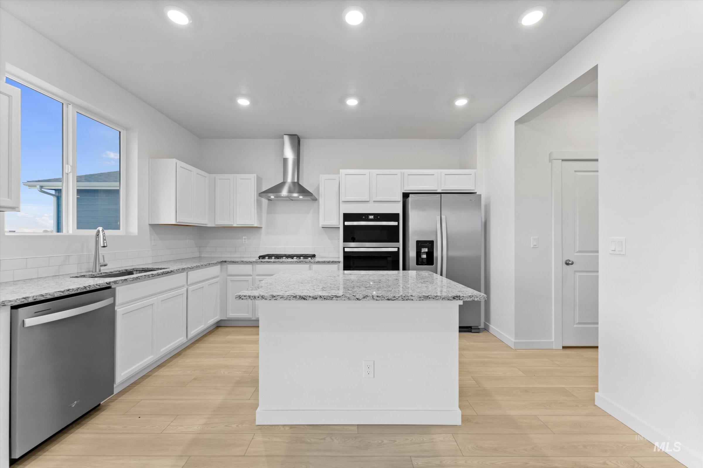 Kitchen with stainless steel appliances, light stone countertops, white cabinets, a center island, and light wood-style flooring