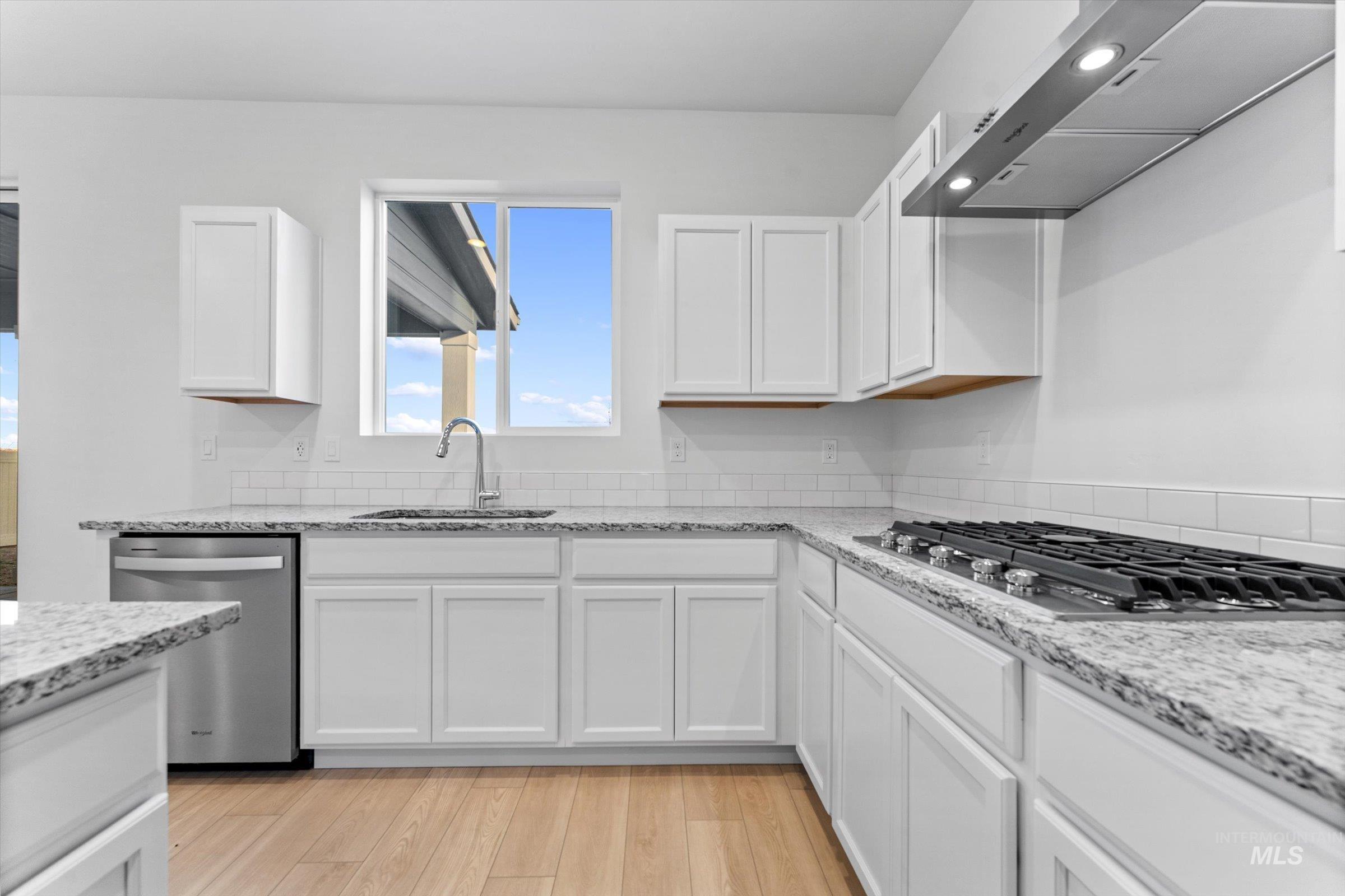 Kitchen with range hood, white cabinetry, light stone counters, stainless steel appliances, and light wood-style floors