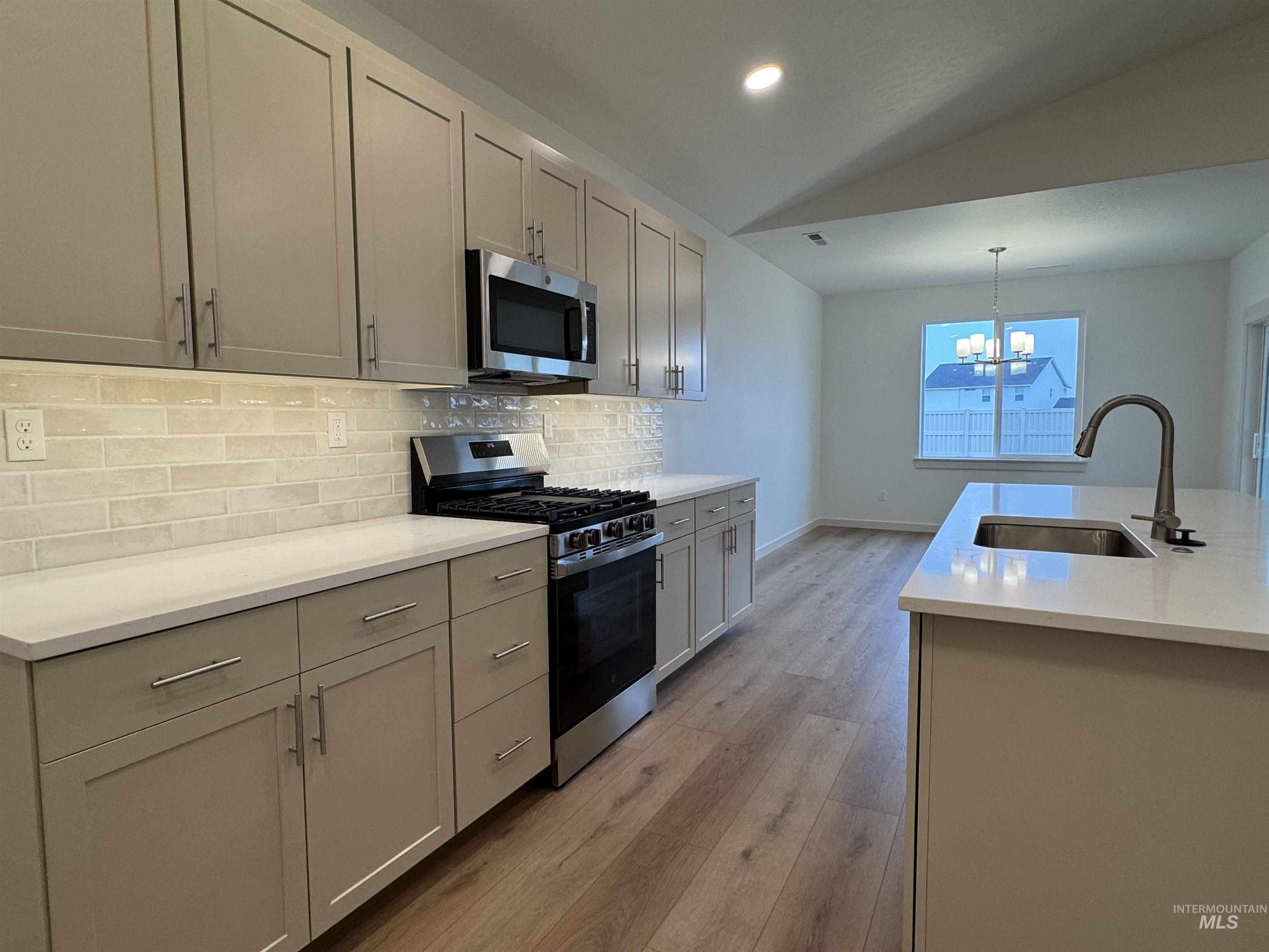 Kitchen with appliances with stainless steel finishes, vaulted ceiling, decorative light fixtures, backsplash, and light wood-type flooring
