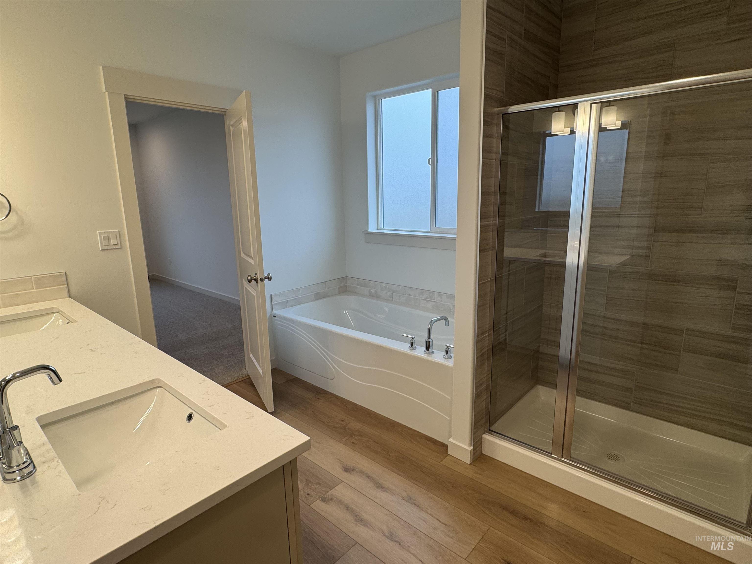 Full bathroom with a stall shower, a garden tub, double vanity, and light wood-style flooring