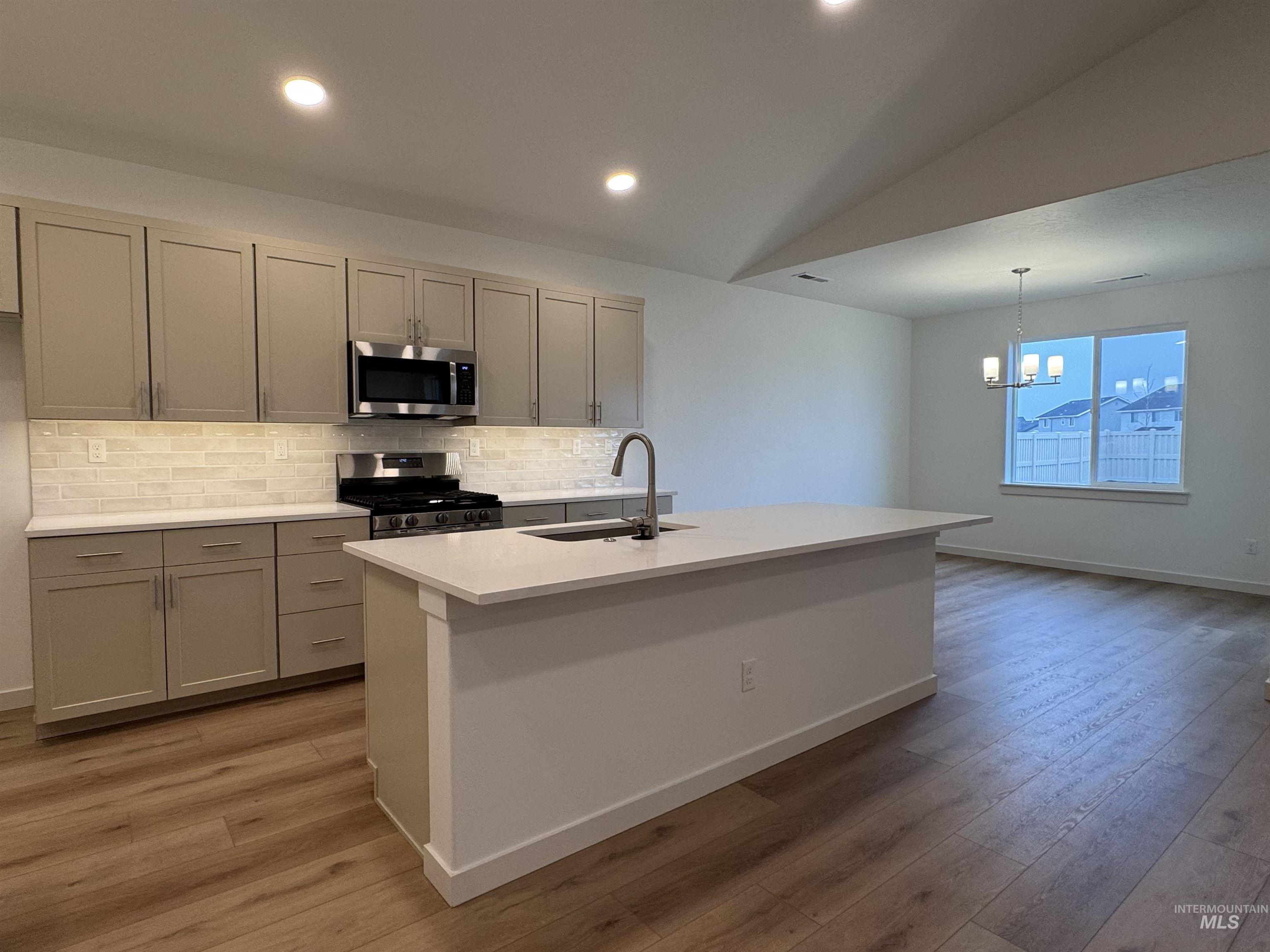 Kitchen featuring vaulted ceiling, appliances with stainless steel finishes, a kitchen island with sink, backsplash, and pendant lighting