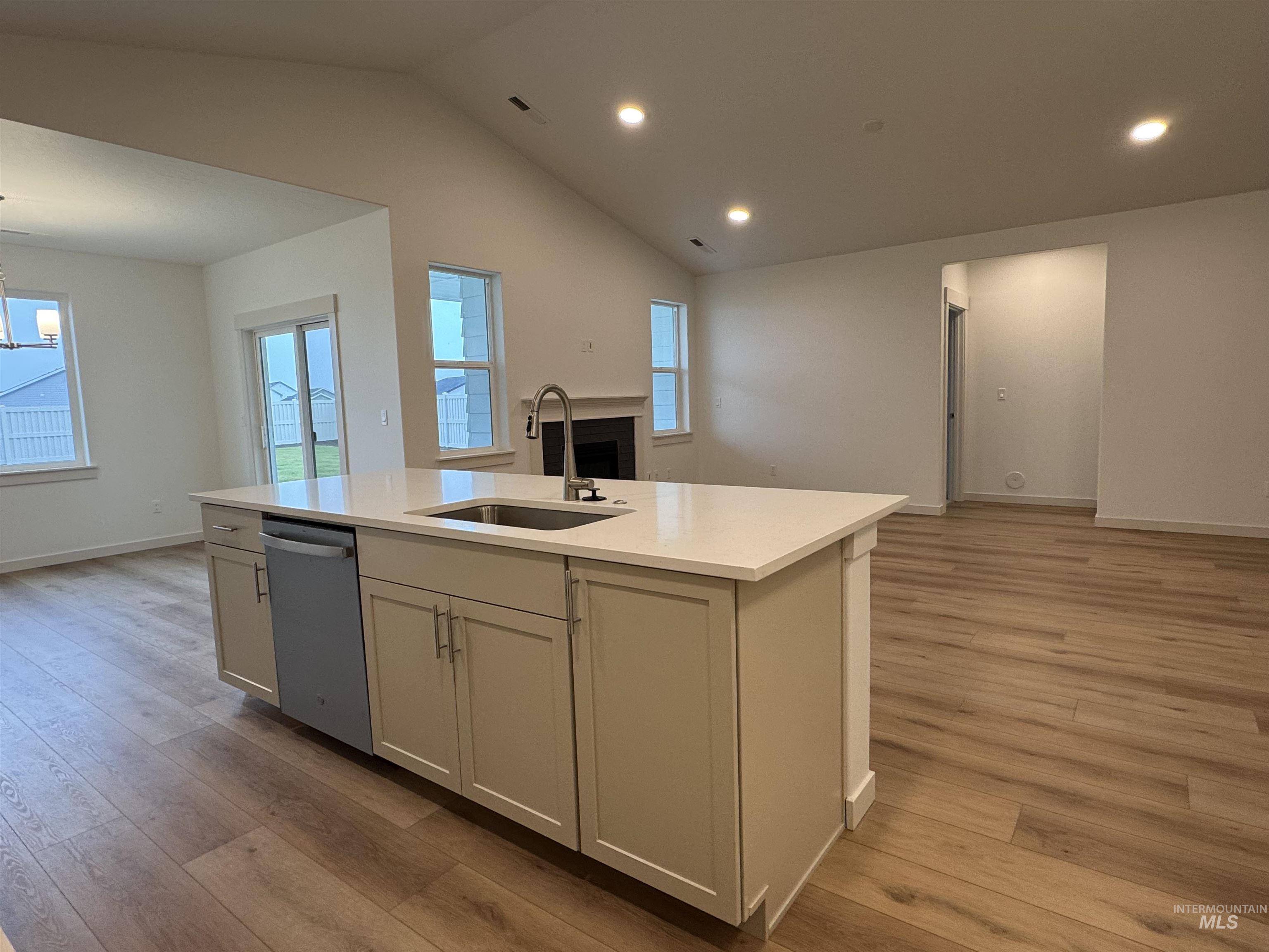 Kitchen with open floor plan, lofted ceiling, dishwasher, light wood-style floors, and light stone counters