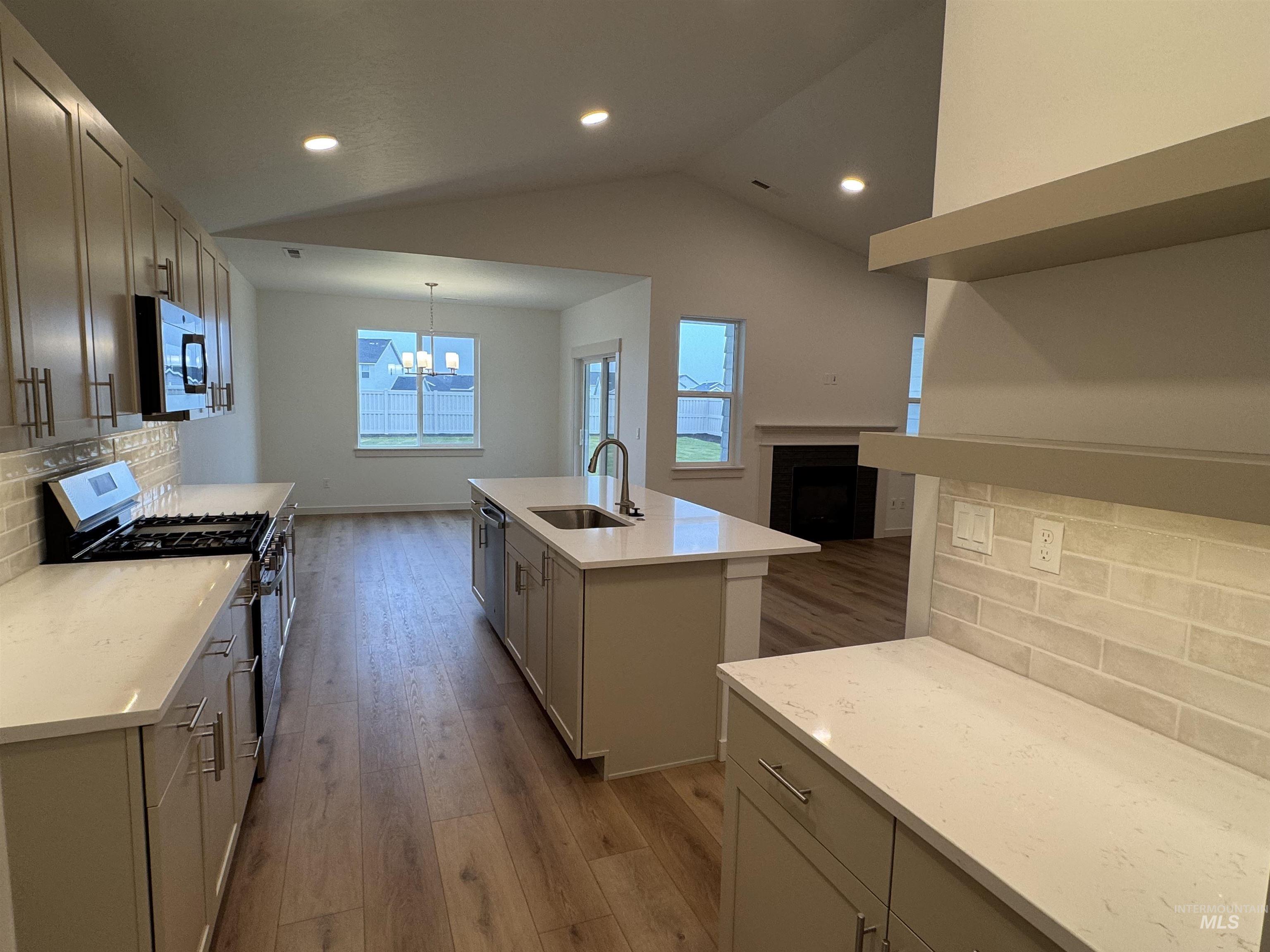 Kitchen featuring tasteful backsplash, appliances with stainless steel finishes, light wood finished floors, a center island with sink, and lofted ceiling