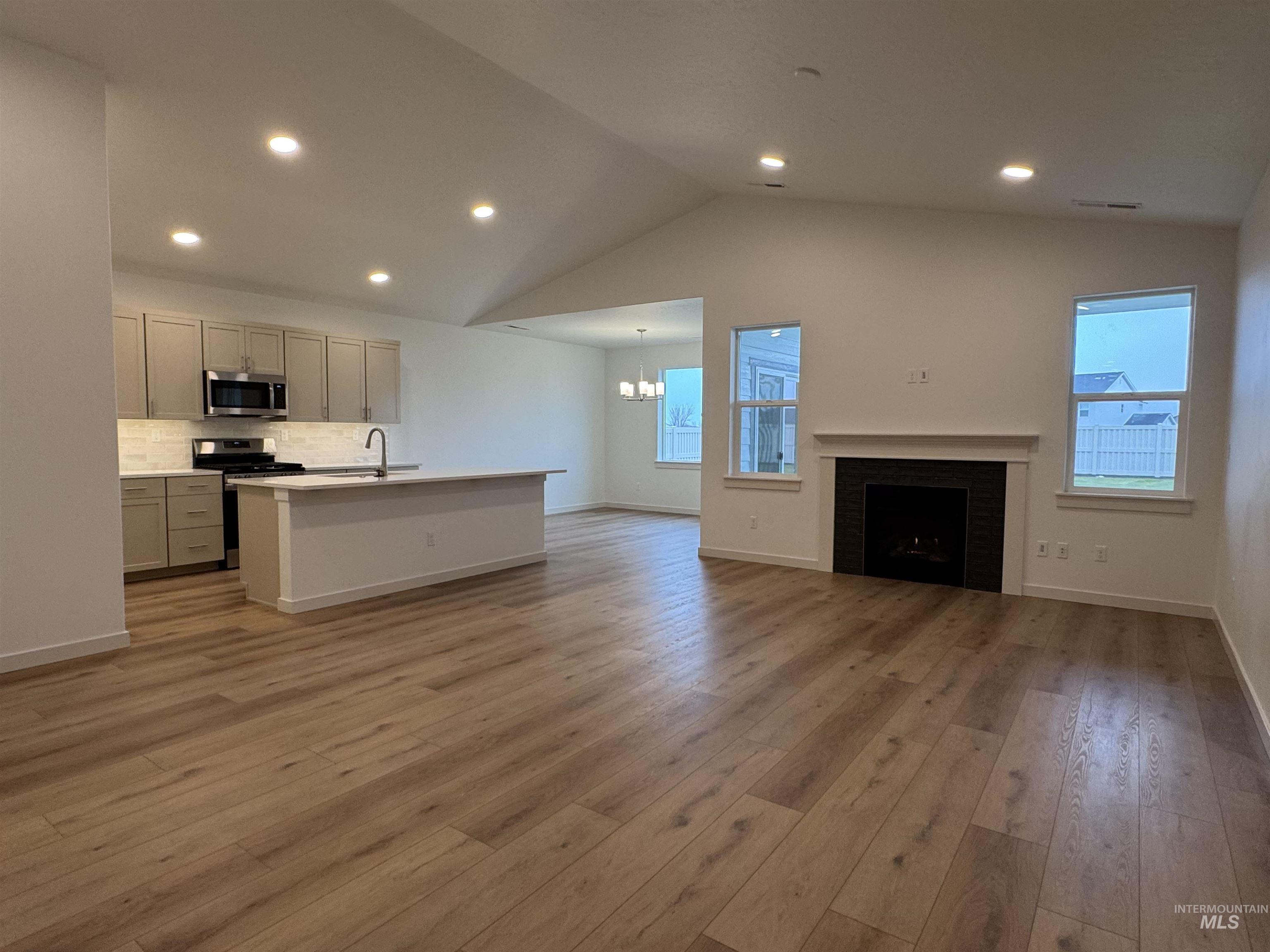 Kitchen featuring open floor plan, a center island with sink, vaulted ceiling, a fireplace, and stainless steel appliances