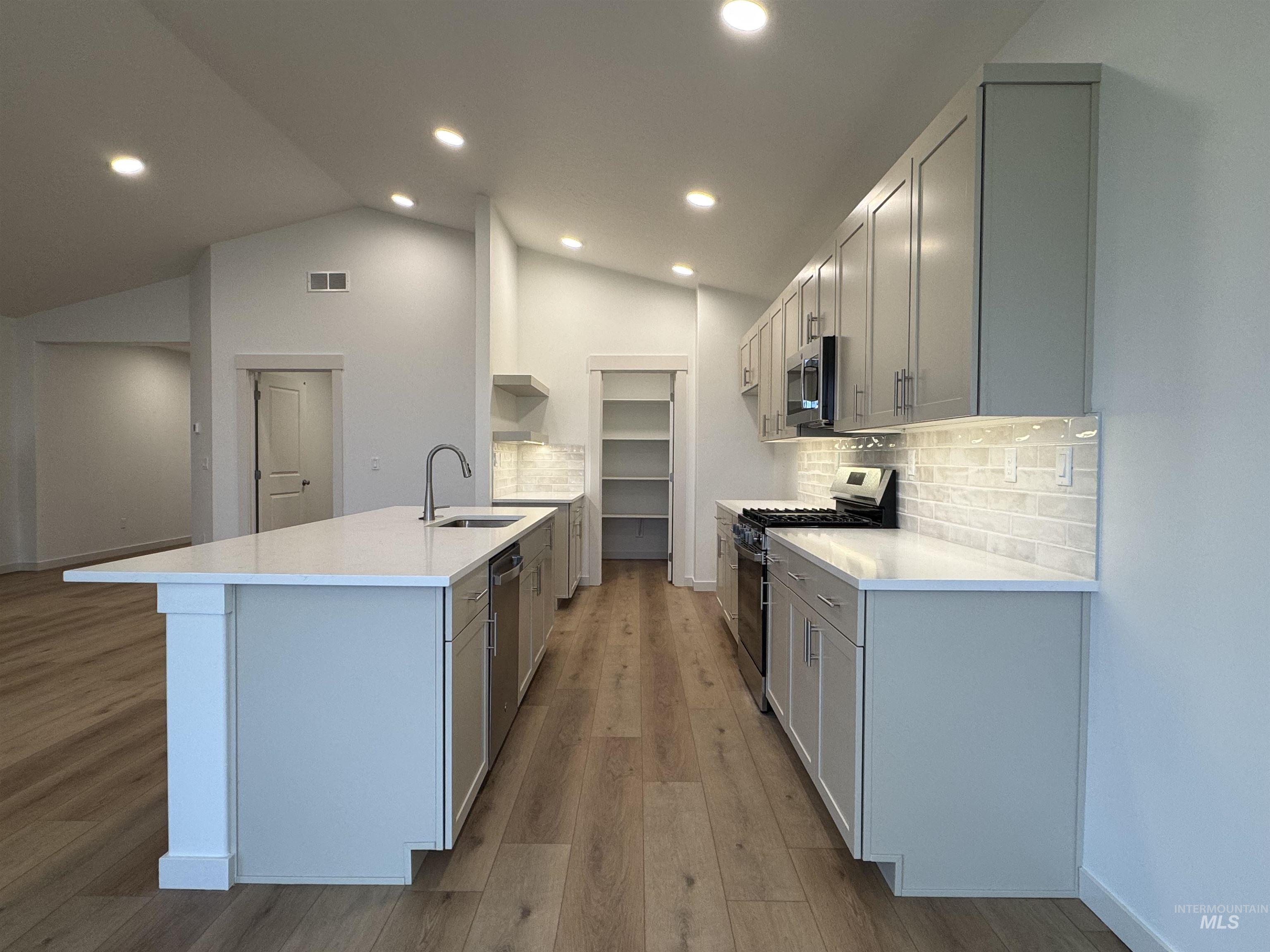 Kitchen featuring stainless steel appliances, backsplash, gray cabinets, light stone counters, and lofted ceiling