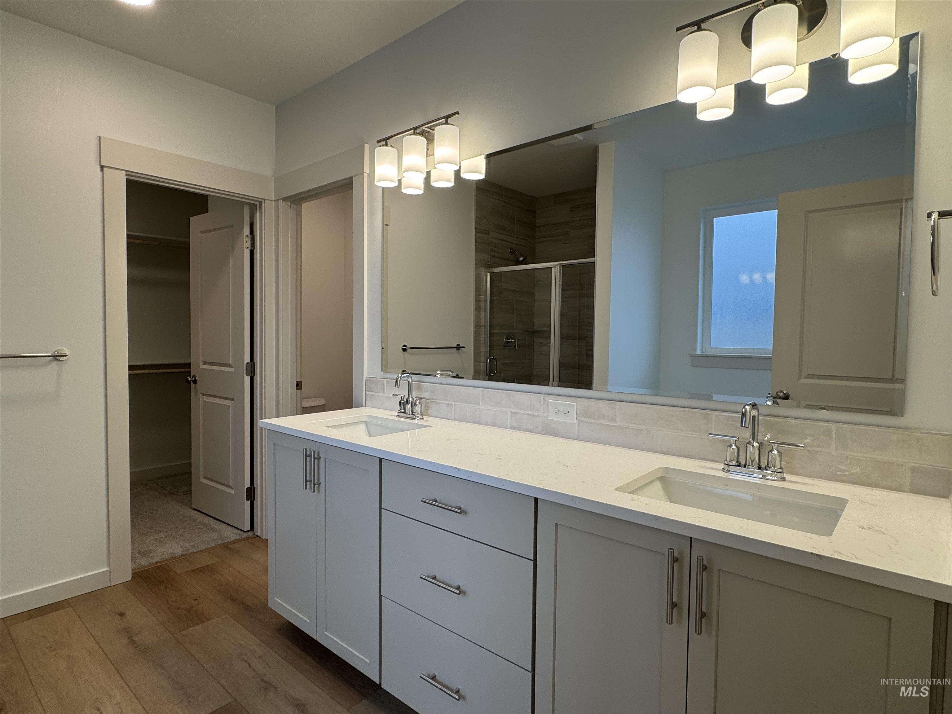 Bathroom with double vanity, a stall shower, light wood-type flooring, and a spacious closet