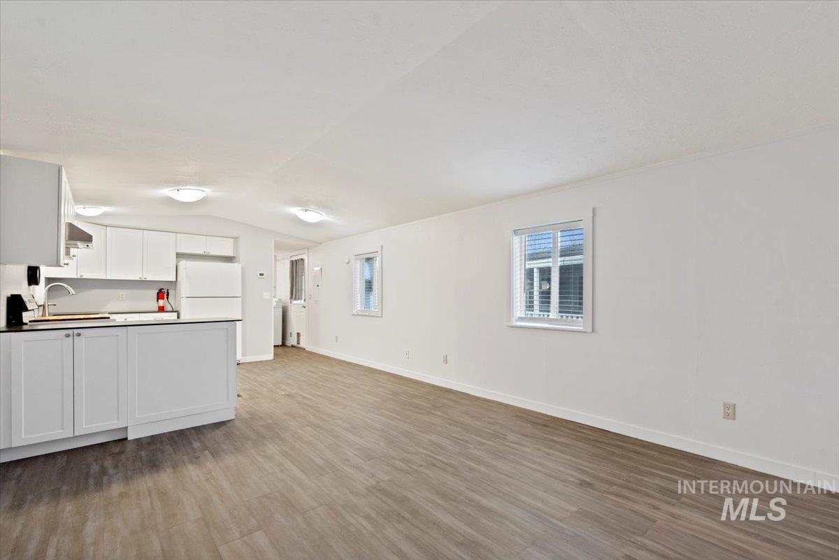 Kitchen featuring white cabinets, lofted ceiling, open floor plan, freestanding refrigerator, and light wood-type flooring