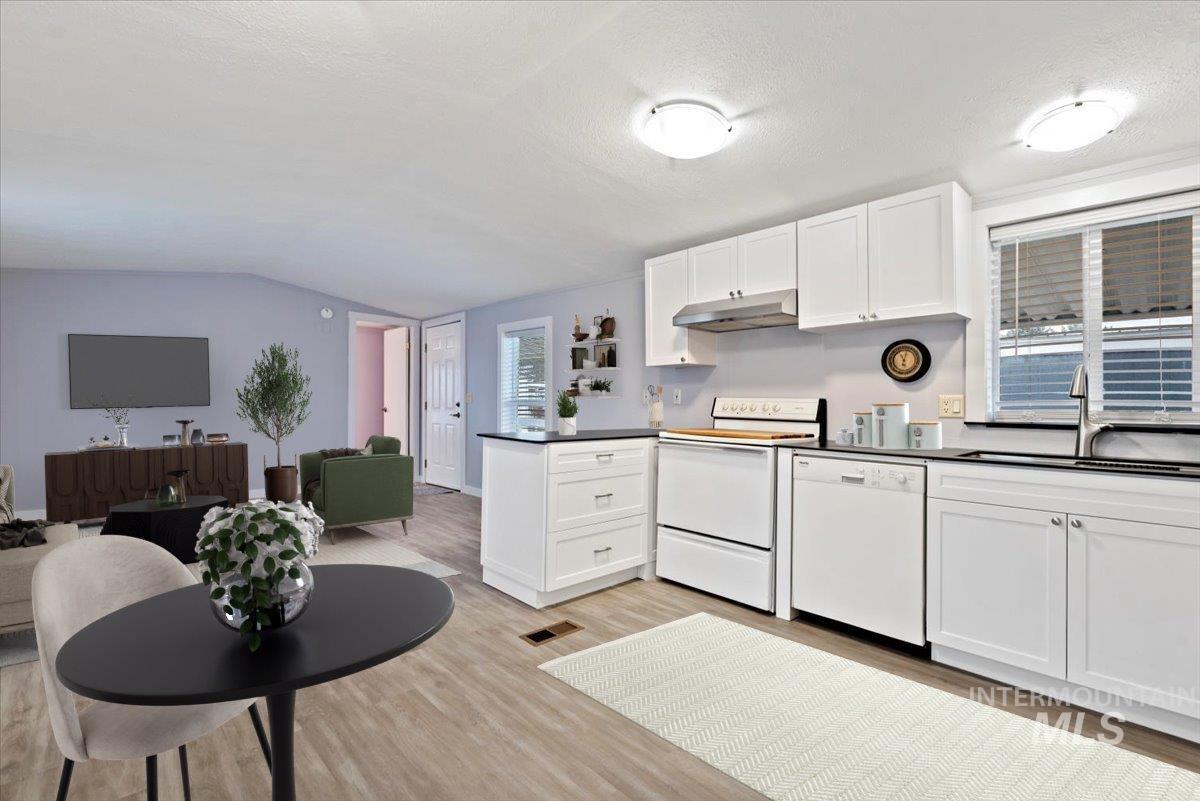 Kitchen featuring white cabinetry, white appliances, a peninsula, open floor plan, and light wood-type flooring