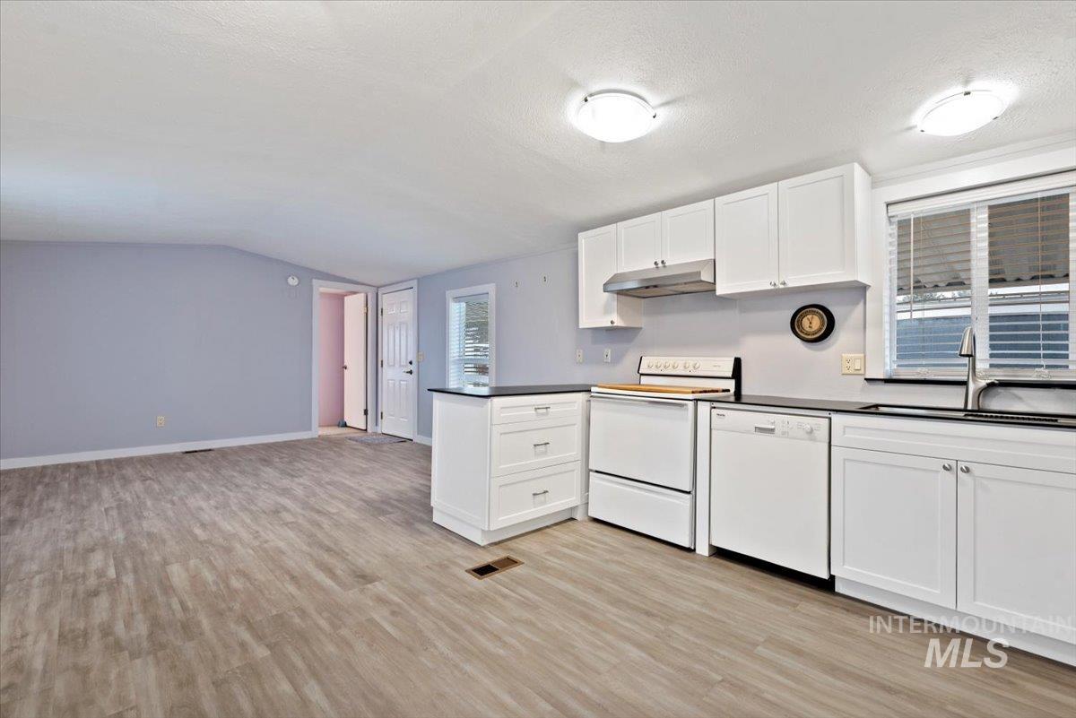 Kitchen with white cabinets, dark countertops, white appliances, vaulted ceiling, and a textured ceiling
