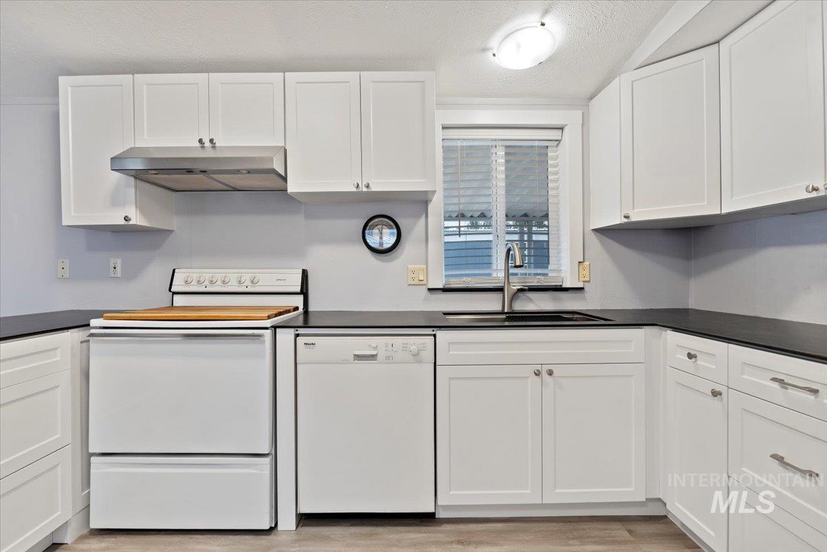 Kitchen with a textured ceiling, white appliances, white cabinets, under cabinet range hood, and light wood finished floors