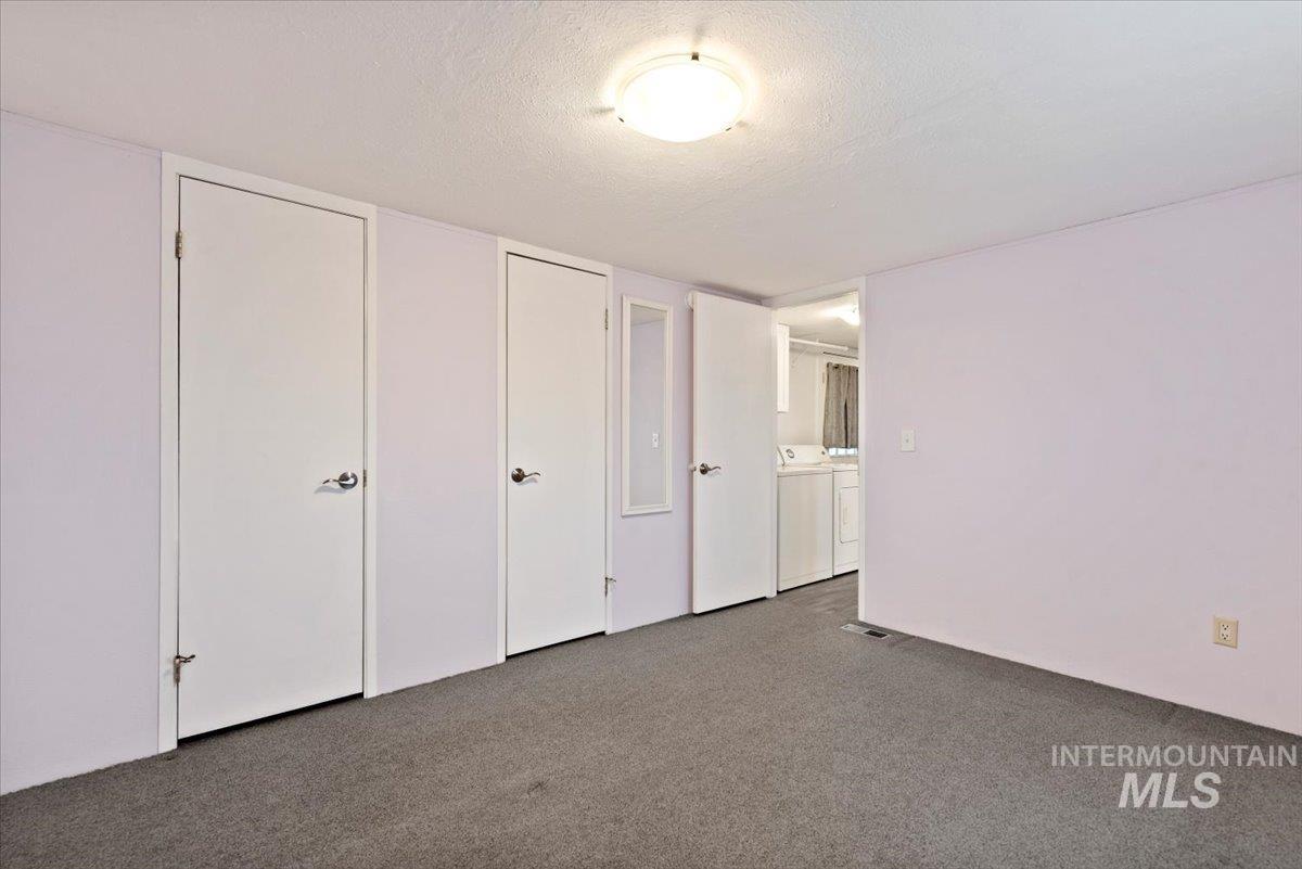 Unfurnished bedroom with a textured ceiling, washing machine and dryer, carpet flooring, and multiple closets