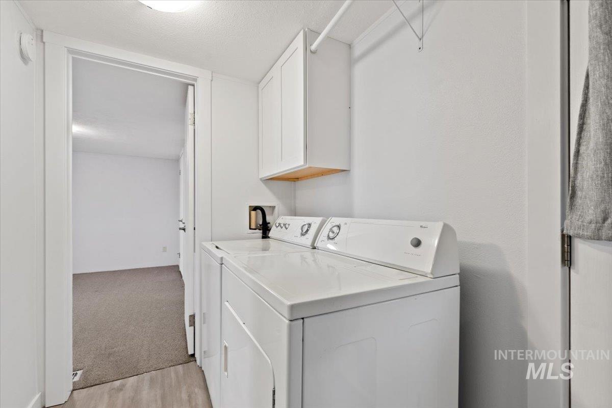 Laundry area with independent washer and dryer, cabinet space, light carpet, and a textured ceiling