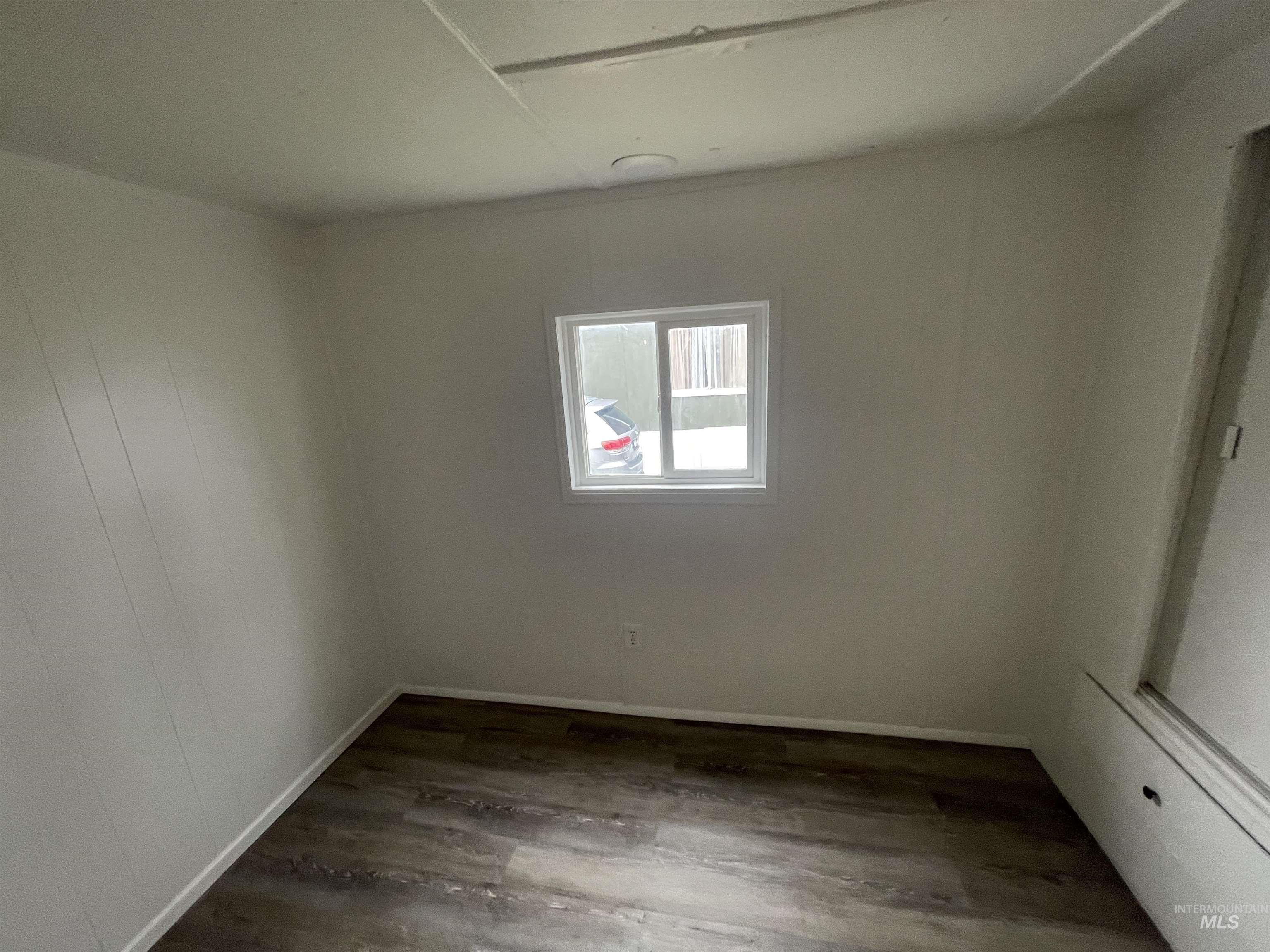 Spare room with dark wood-type flooring and baseboards