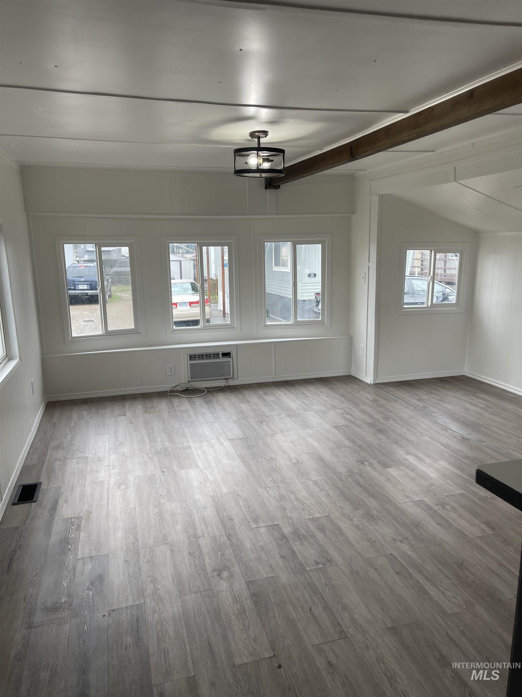 Unfurnished living room featuring light wood-style floors and beamed ceiling