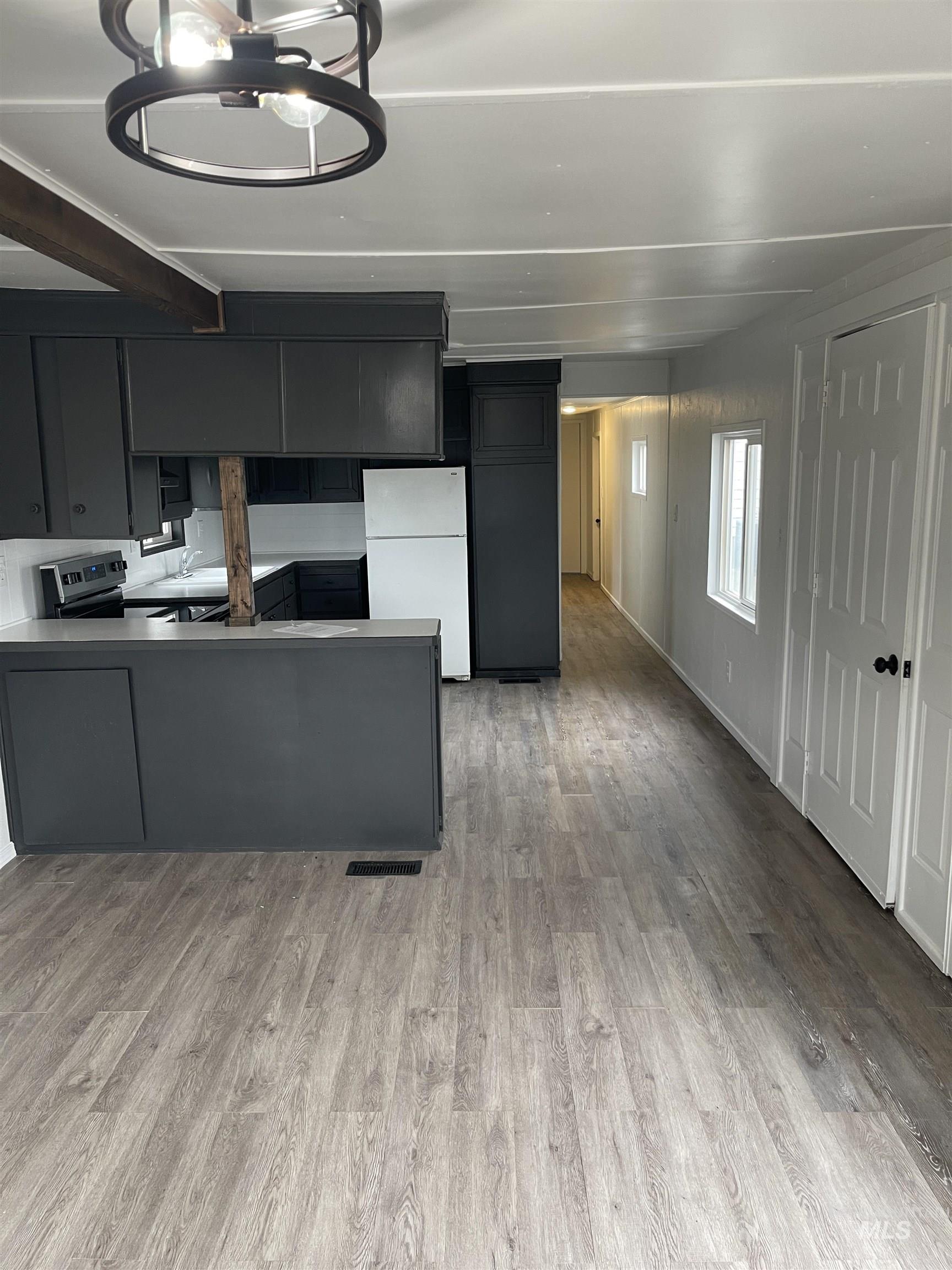 Kitchen featuring dark cabinets, freestanding refrigerator, a peninsula, stainless steel stove, and light wood-style flooring