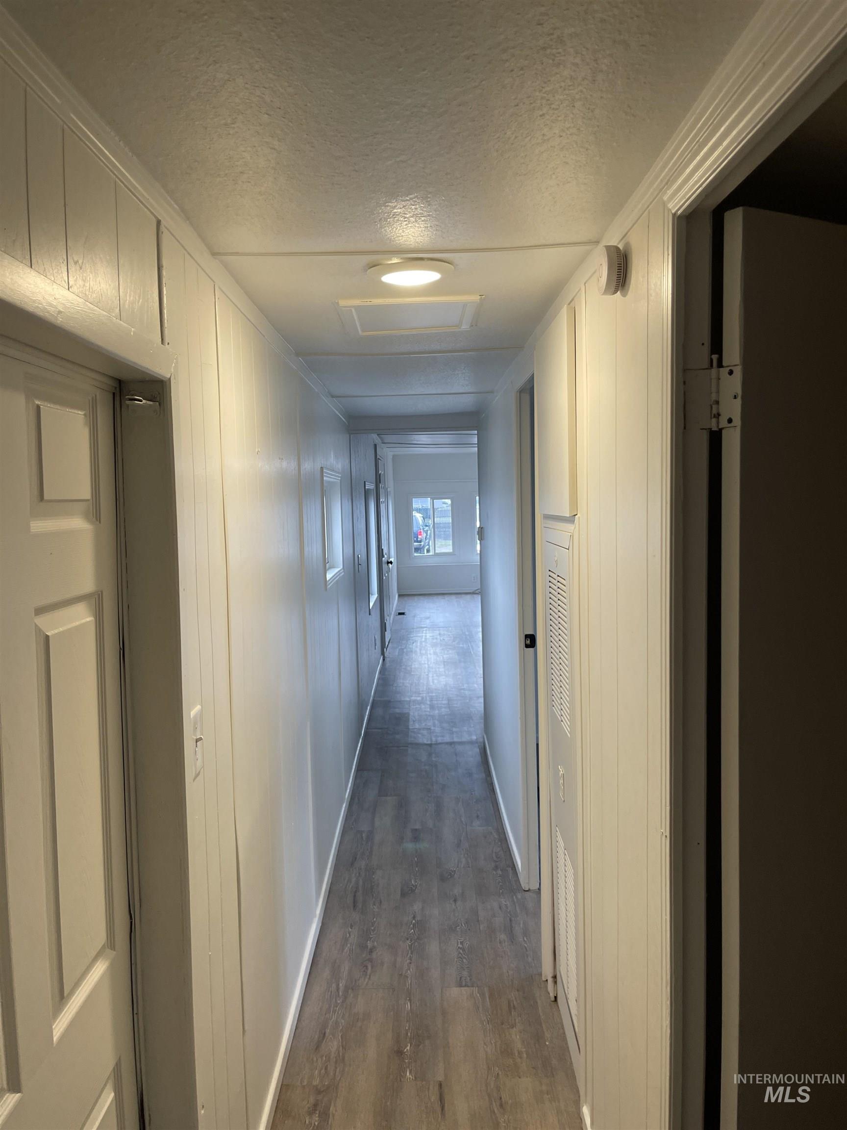 Hall with a textured ceiling, dark wood-type flooring, and attic access