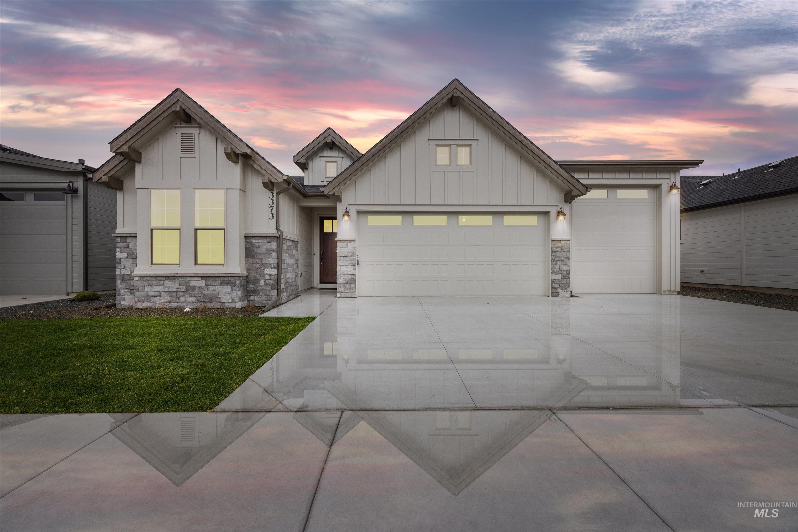 View of front of home with board and batten siding, concrete driveway, stone siding, an attached garage, and a yard
