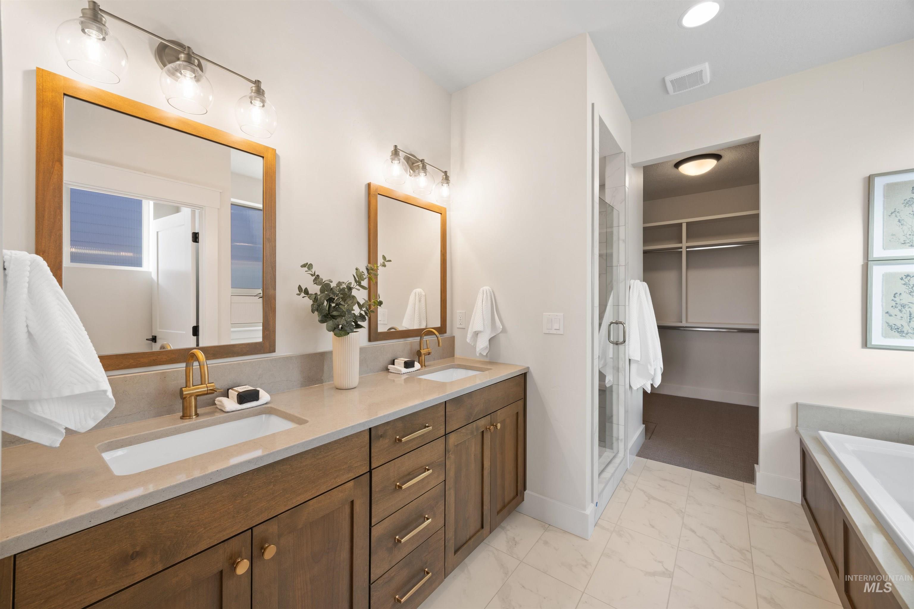 Full bathroom featuring a spacious closet, double vanity, light marble finish floors, a tub to relax in, and a stall shower