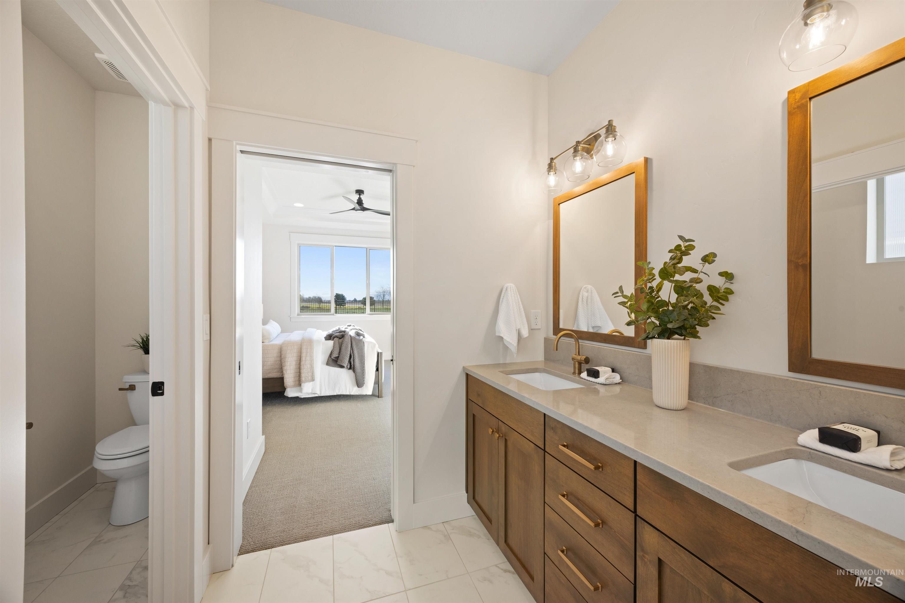 Full bathroom with double vanity, light marble finish floors, connected bathroom, and ceiling fan