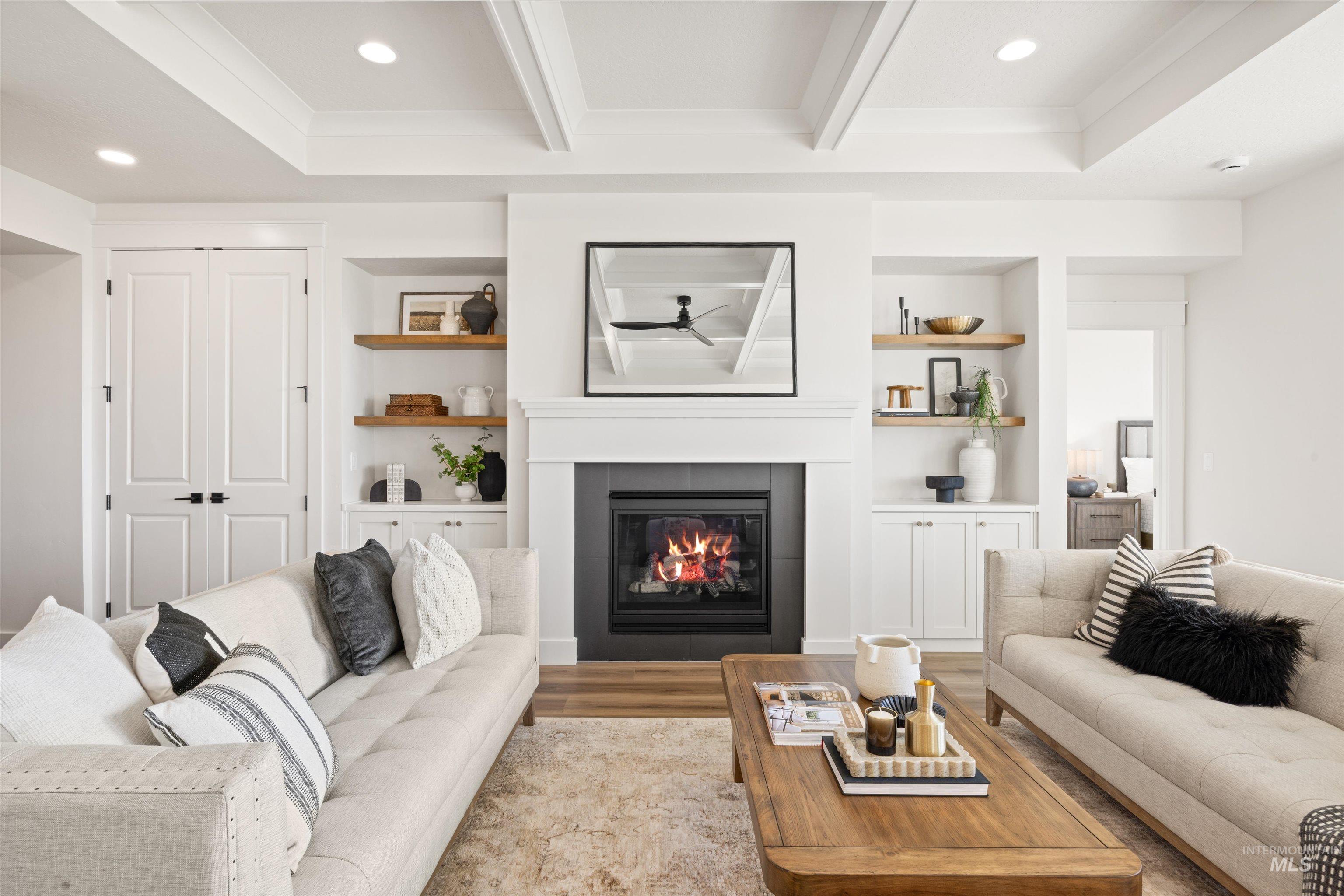 Living area featuring built in shelves, a glass covered fireplace, wood finished floors, beam ceiling, and recessed lighting