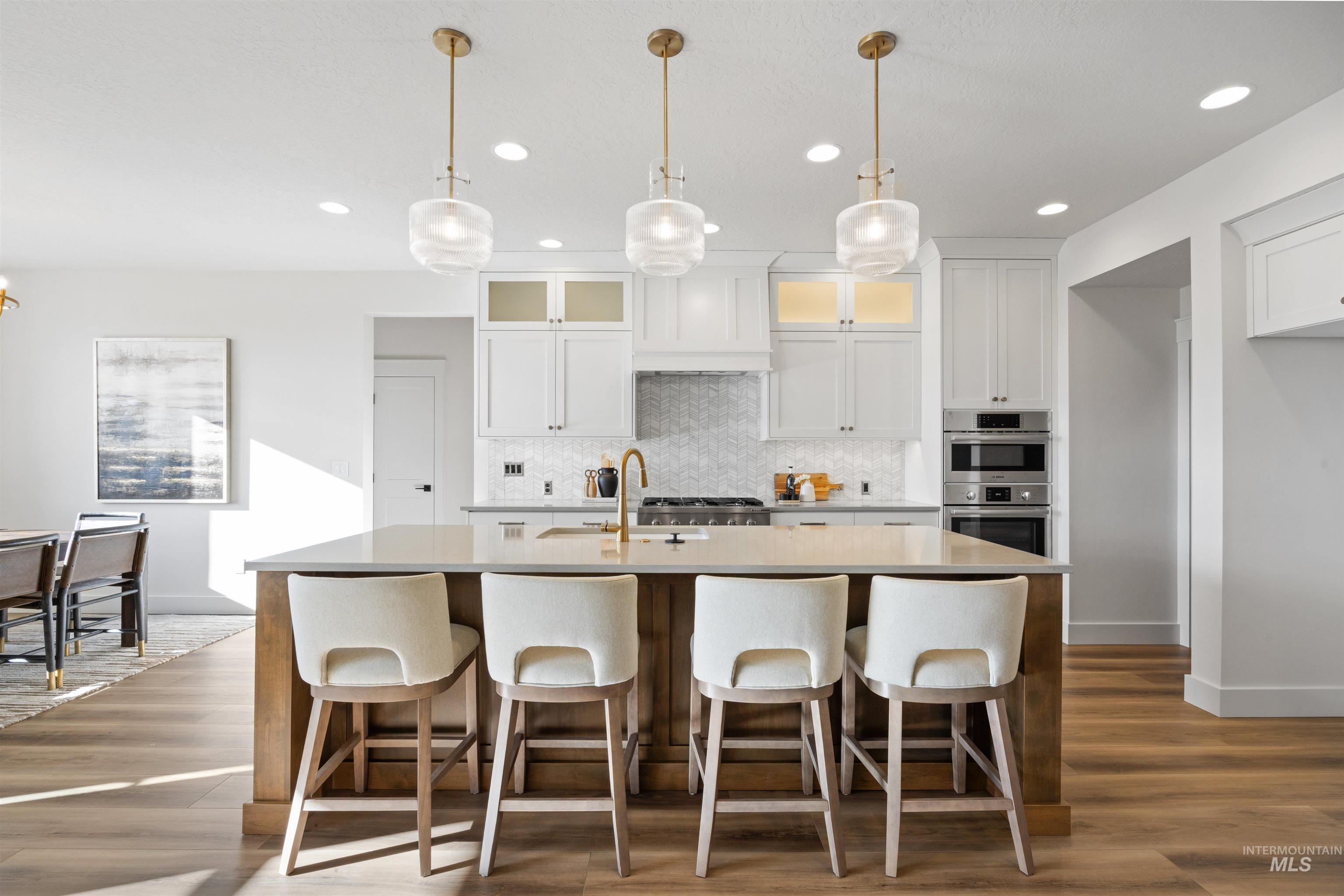 Kitchen with white cabinets, a kitchen breakfast bar, glass insert cabinets, hanging light fixtures, and recessed lighting