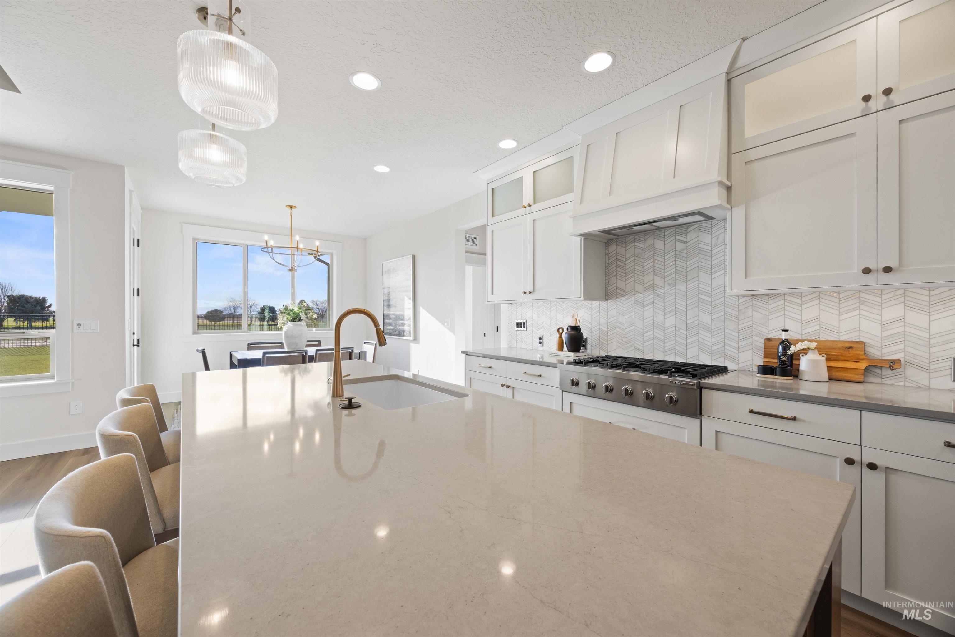 Kitchen featuring decorative backsplash, a breakfast bar area, hanging light fixtures, white cabinetry, and dark stone counters