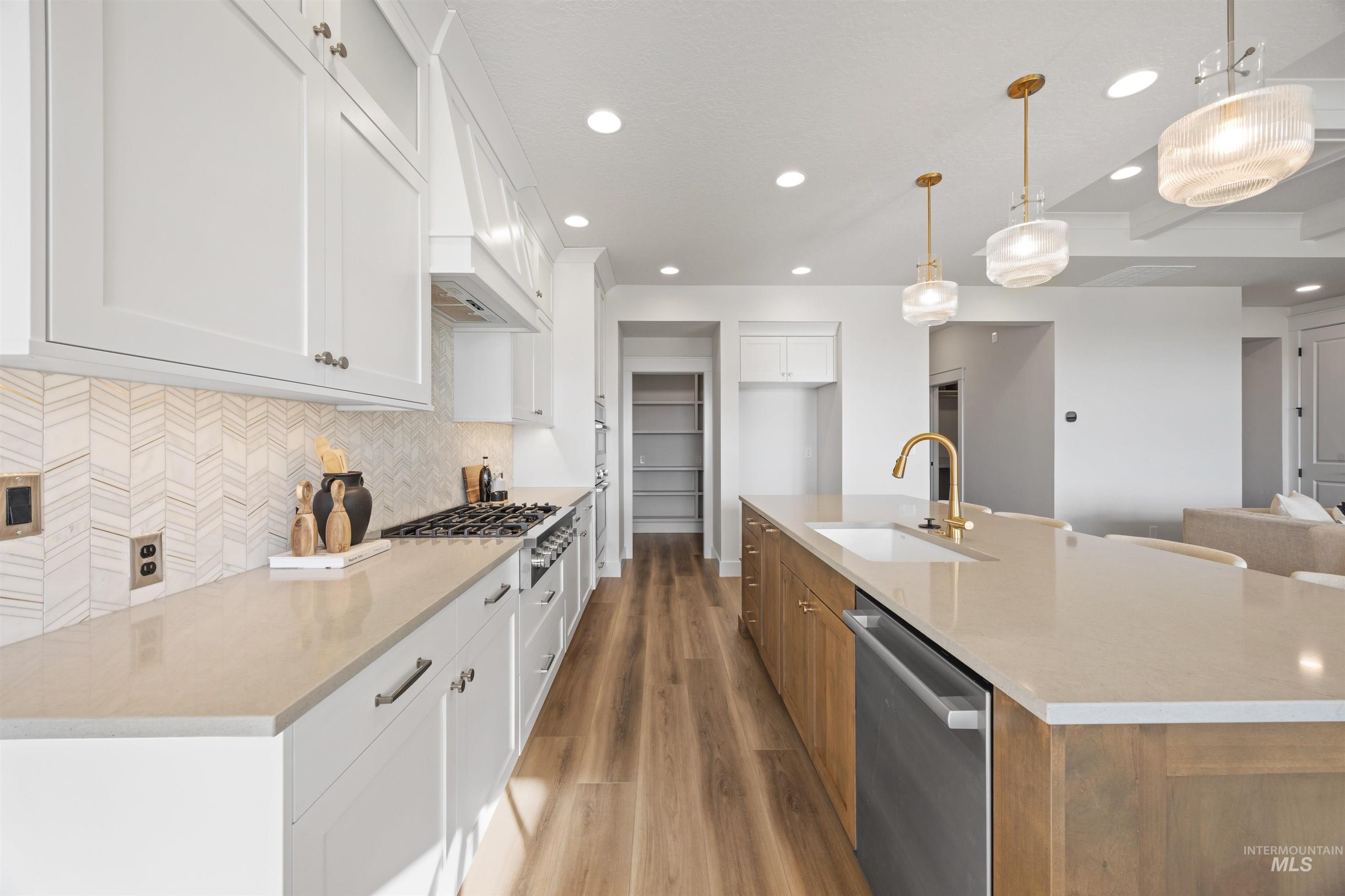 Kitchen with white cabinets, appliances with stainless steel finishes, pendant lighting, light stone countertops, and decorative backsplash