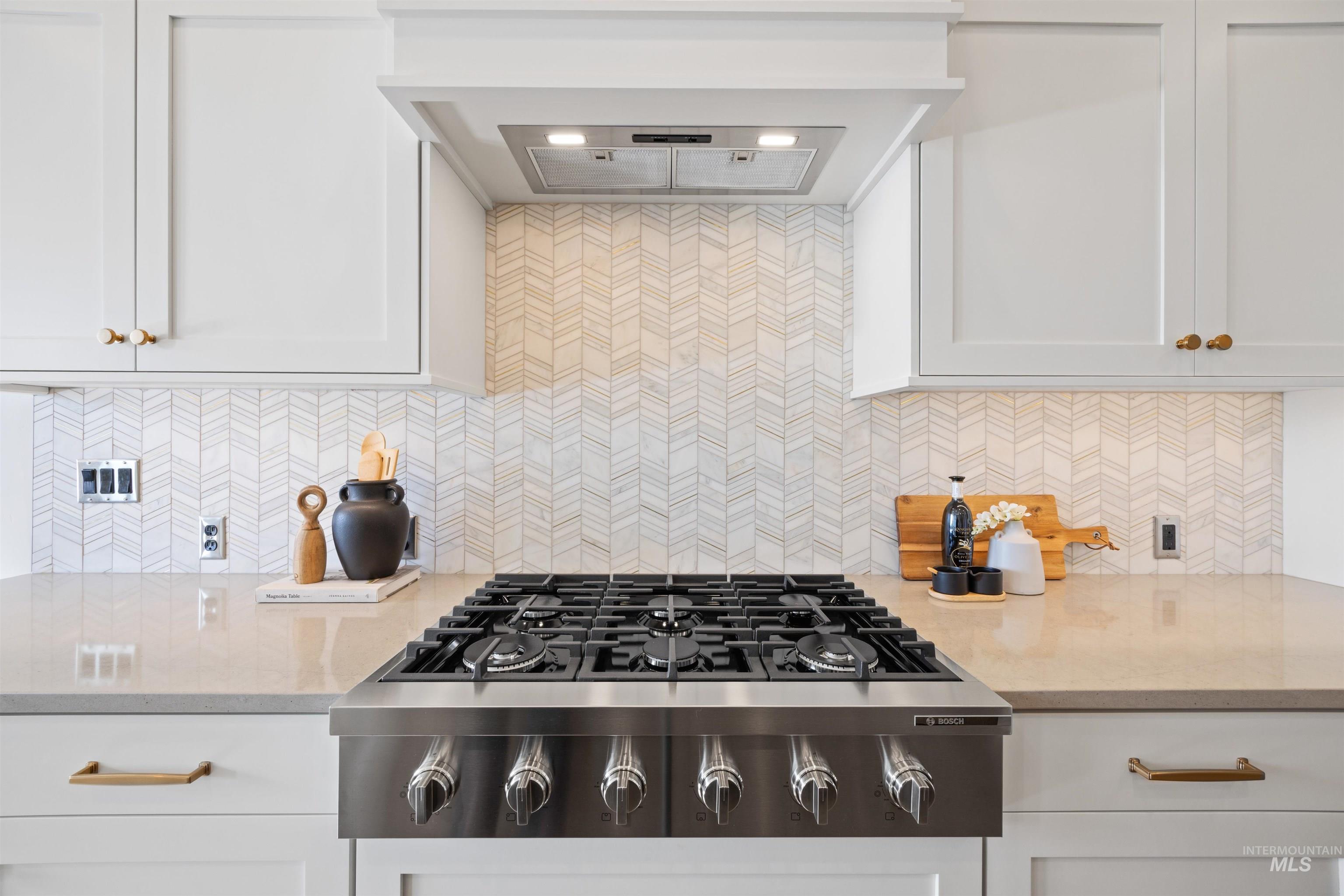 Kitchen featuring extractor fan, light stone counters, stainless steel gas cooktop, and tasteful backsplash
