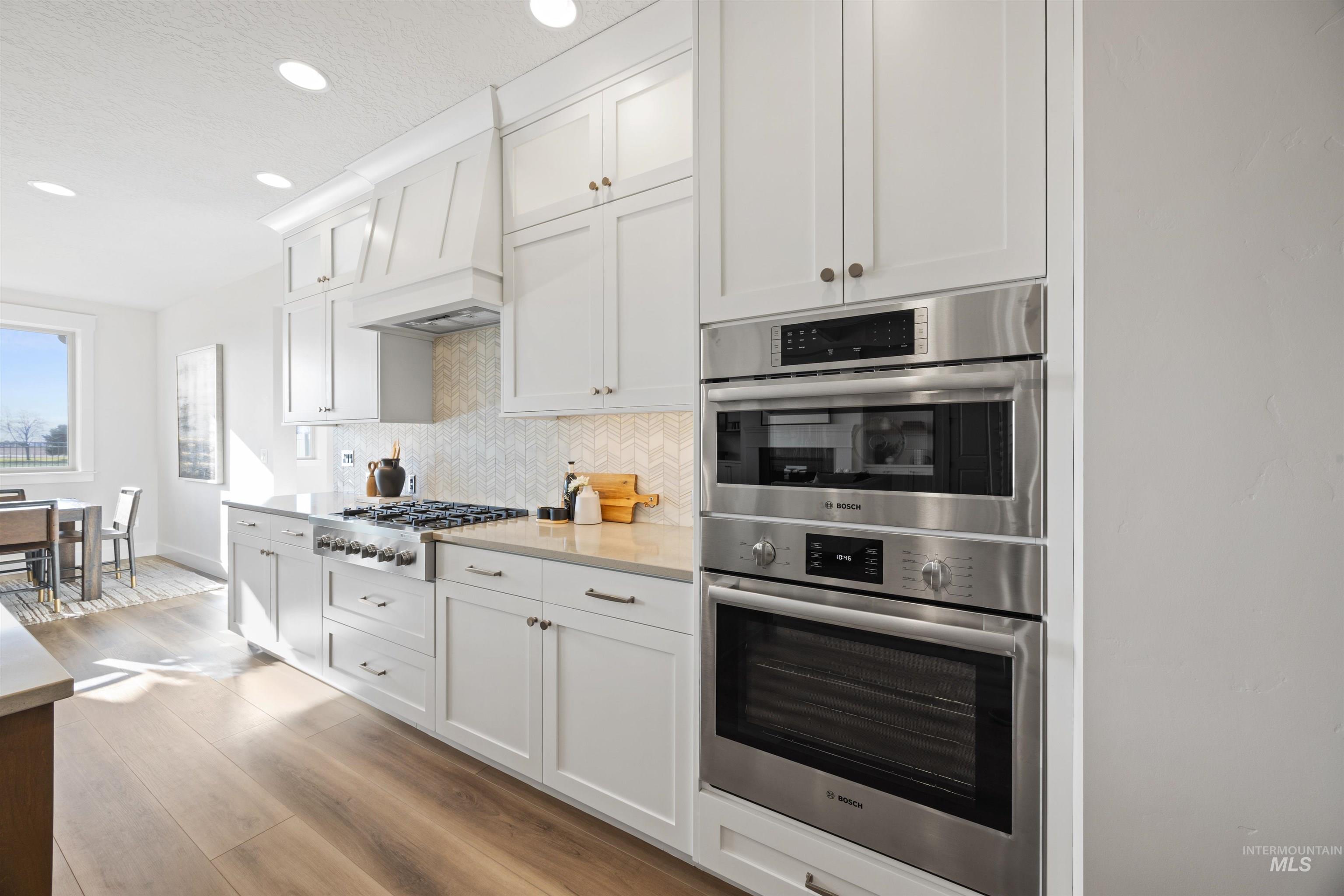 Kitchen featuring appliances with stainless steel finishes, white cabinetry, backsplash, recessed lighting, and light wood finished floors