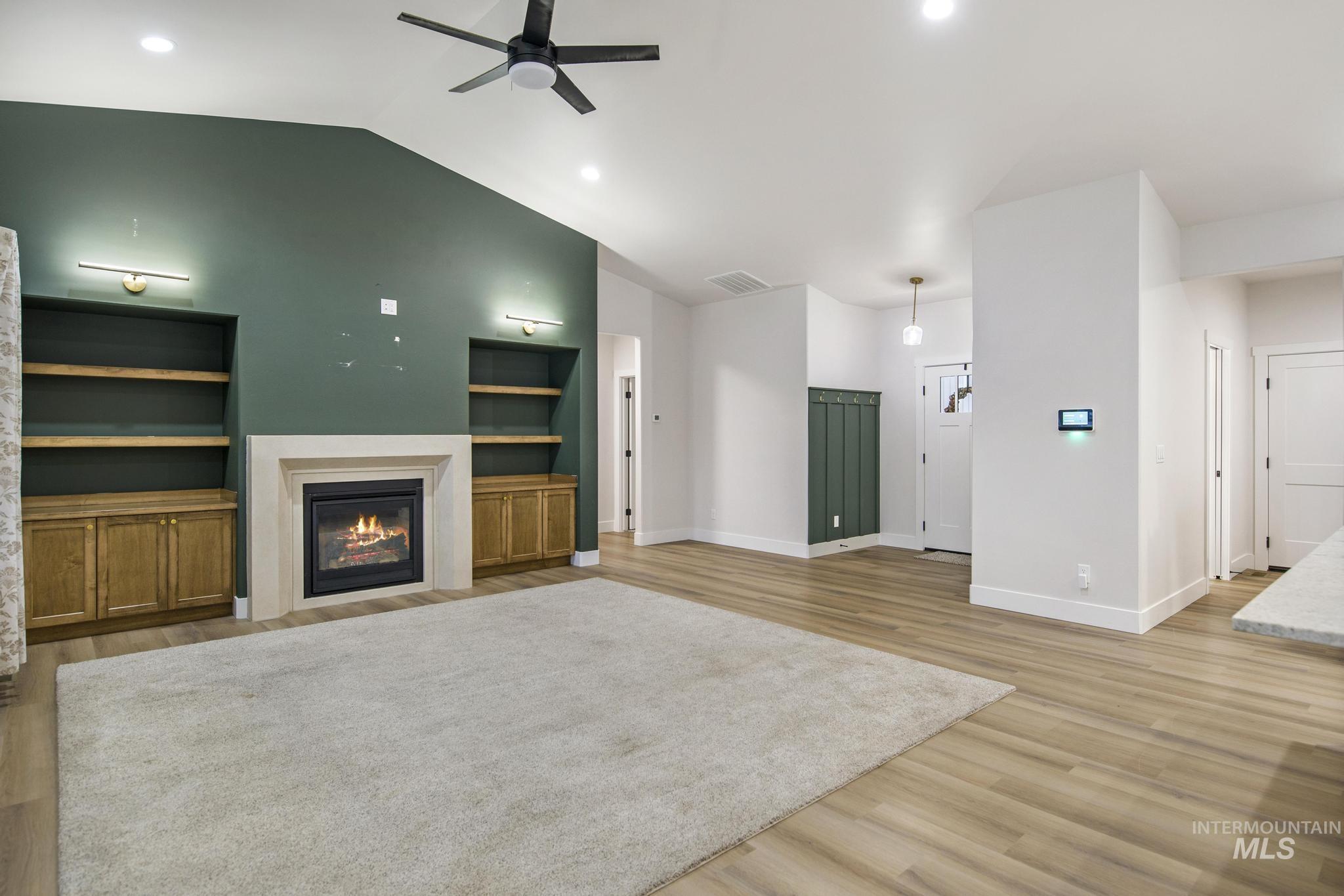 Unfurnished living room featuring light wood finished floors, lofted ceiling, a glass covered fireplace, ceiling fan, and recessed lighting