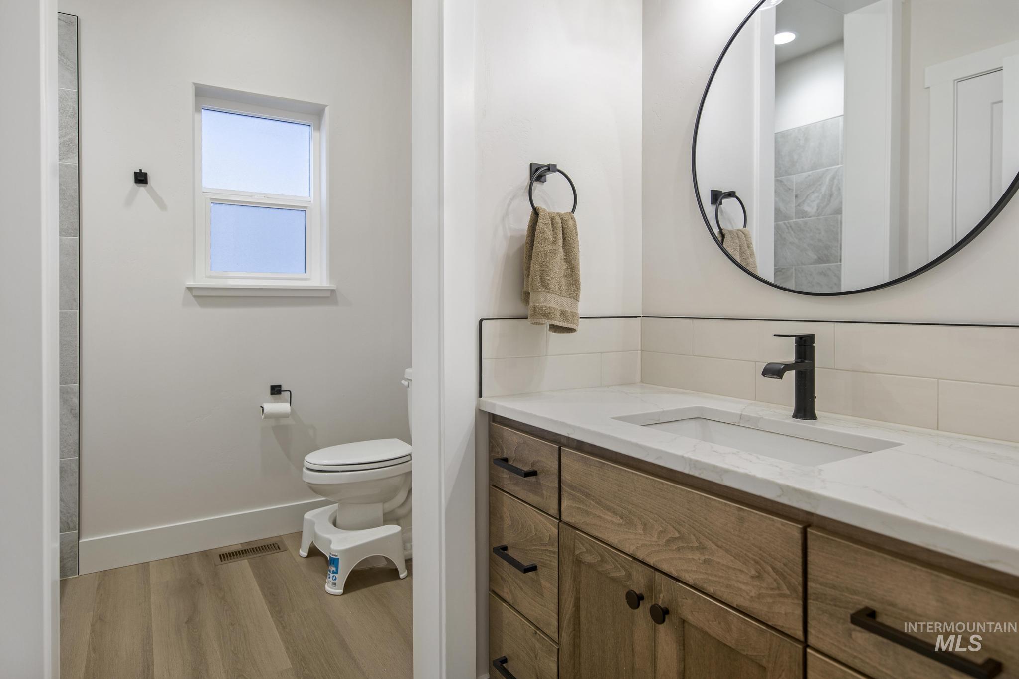 Full bathroom with vanity, light wood-type flooring, and backsplash