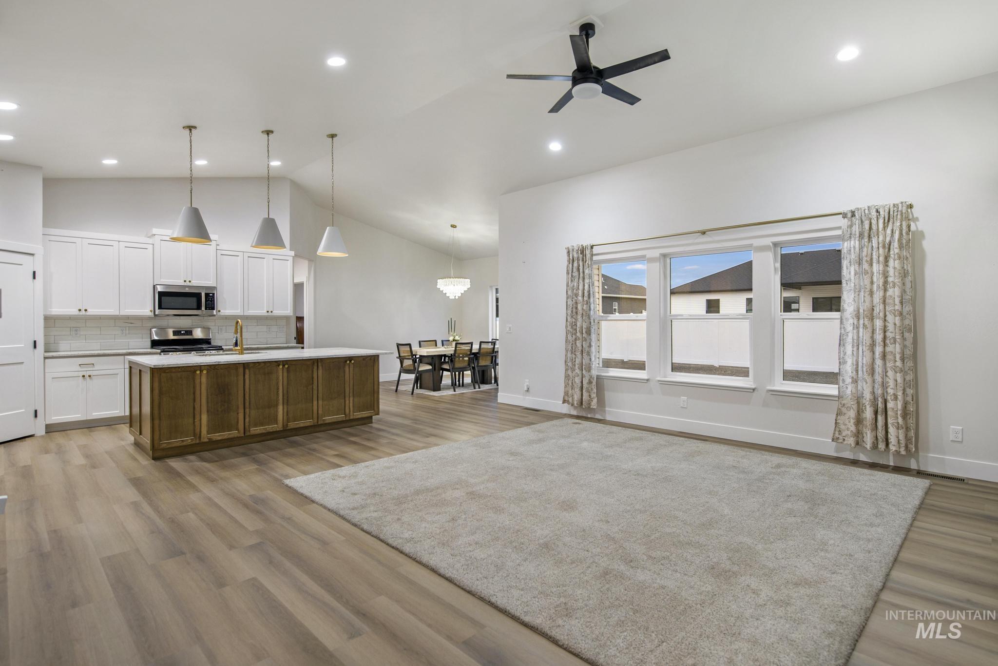 Kitchen featuring white cabinetry, open floor plan, a kitchen island with sink, pendant lighting, and vaulted ceiling