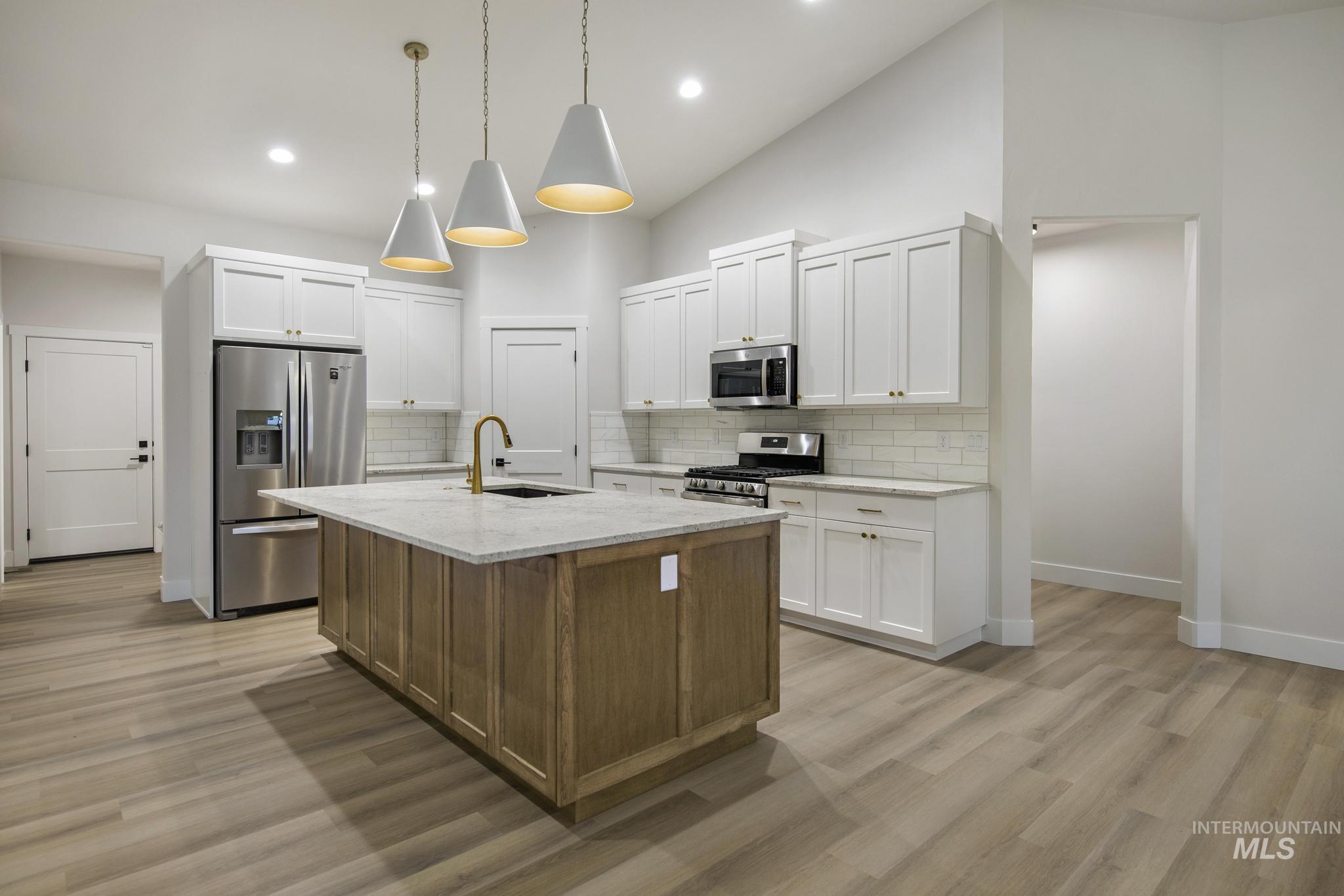Kitchen with white cabinetry, stainless steel appliances, an island with sink, recessed lighting, and high vaulted ceiling