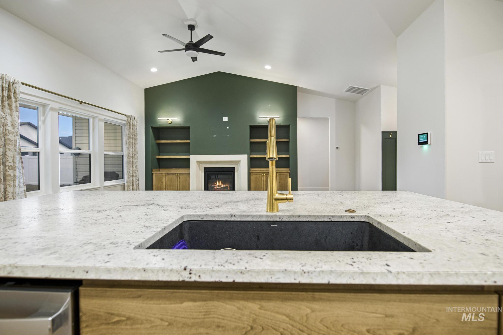 Kitchen with light stone counters, lofted ceiling, recessed lighting, stainless steel dishwasher, and a glass covered fireplace