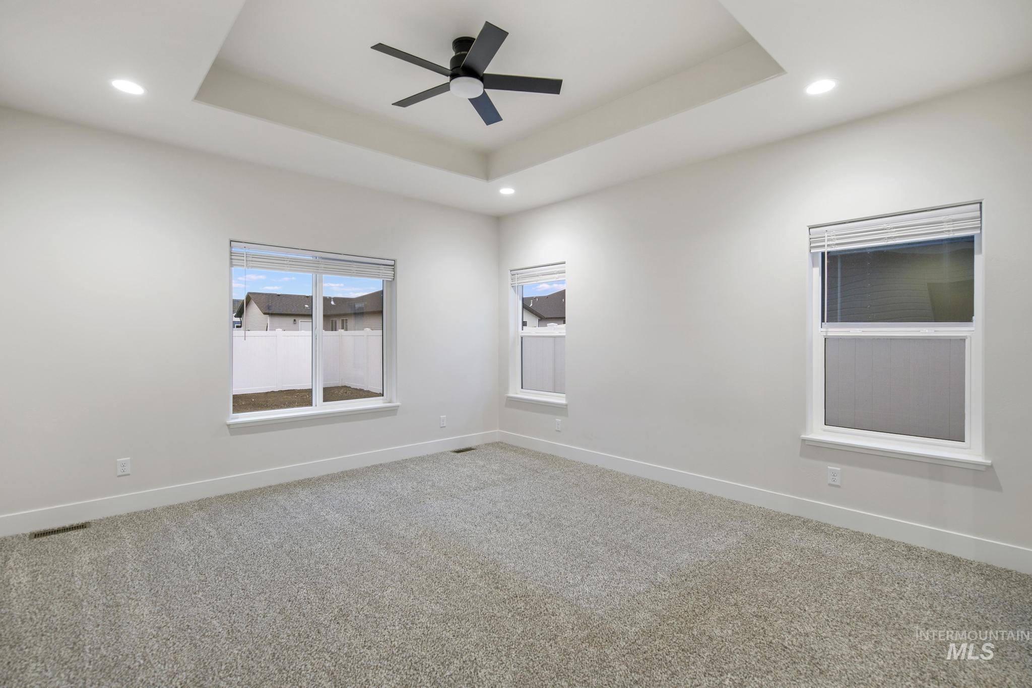 Carpeted empty room featuring a raised ceiling, recessed lighting, and a ceiling fan