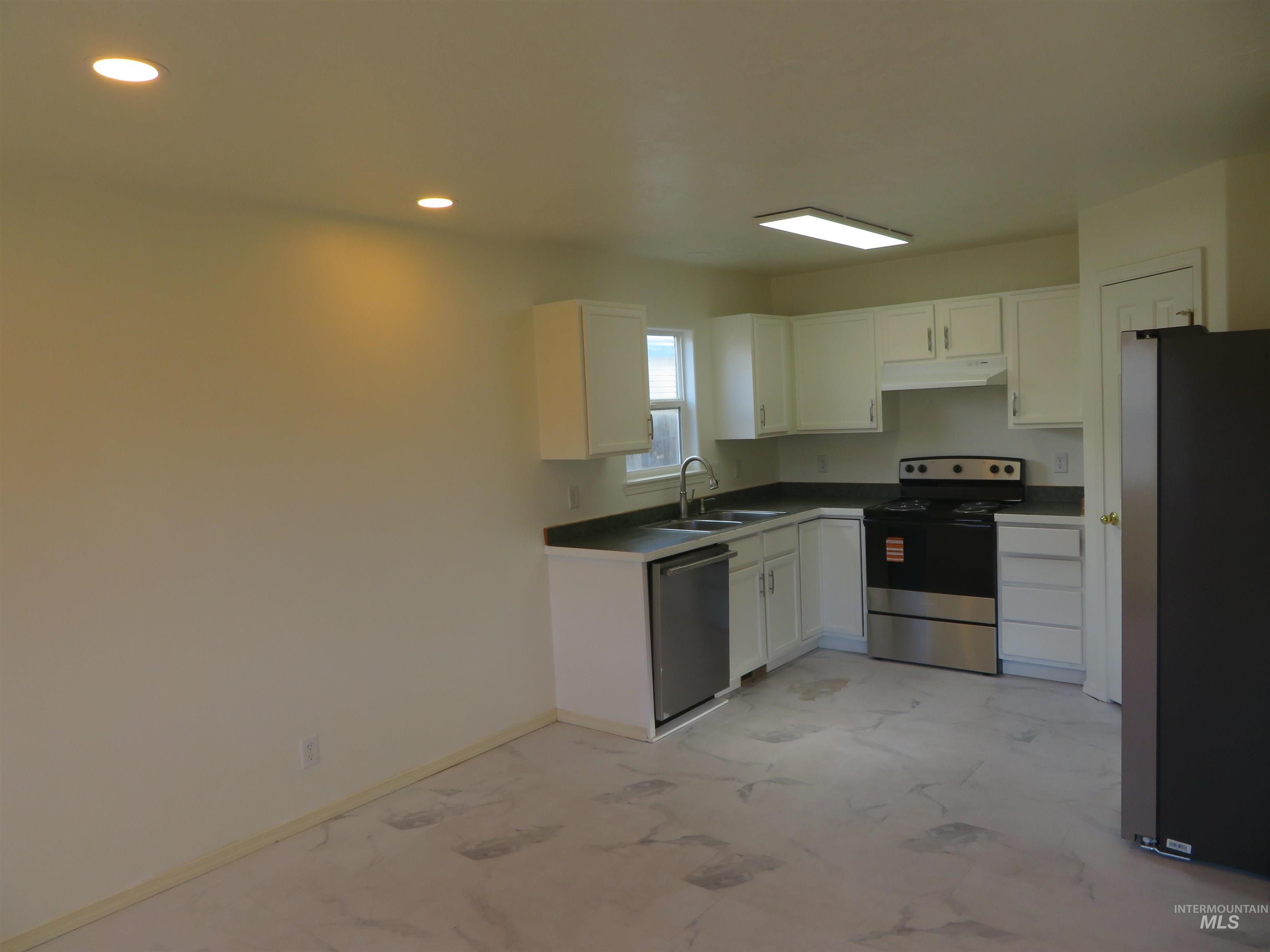 Kitchen with appliances with stainless steel finishes, white cabinets, under cabinet range hood, light marble finish floors, and recessed lighting
