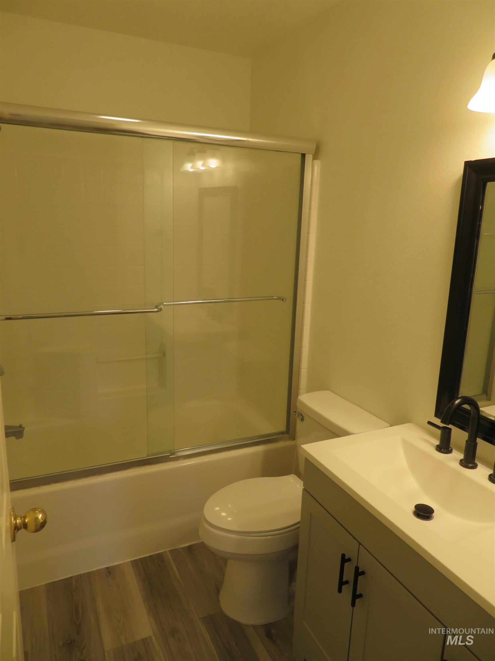 Bathroom with dark wood-style floors, vanity, and enclosed tub / shower combo