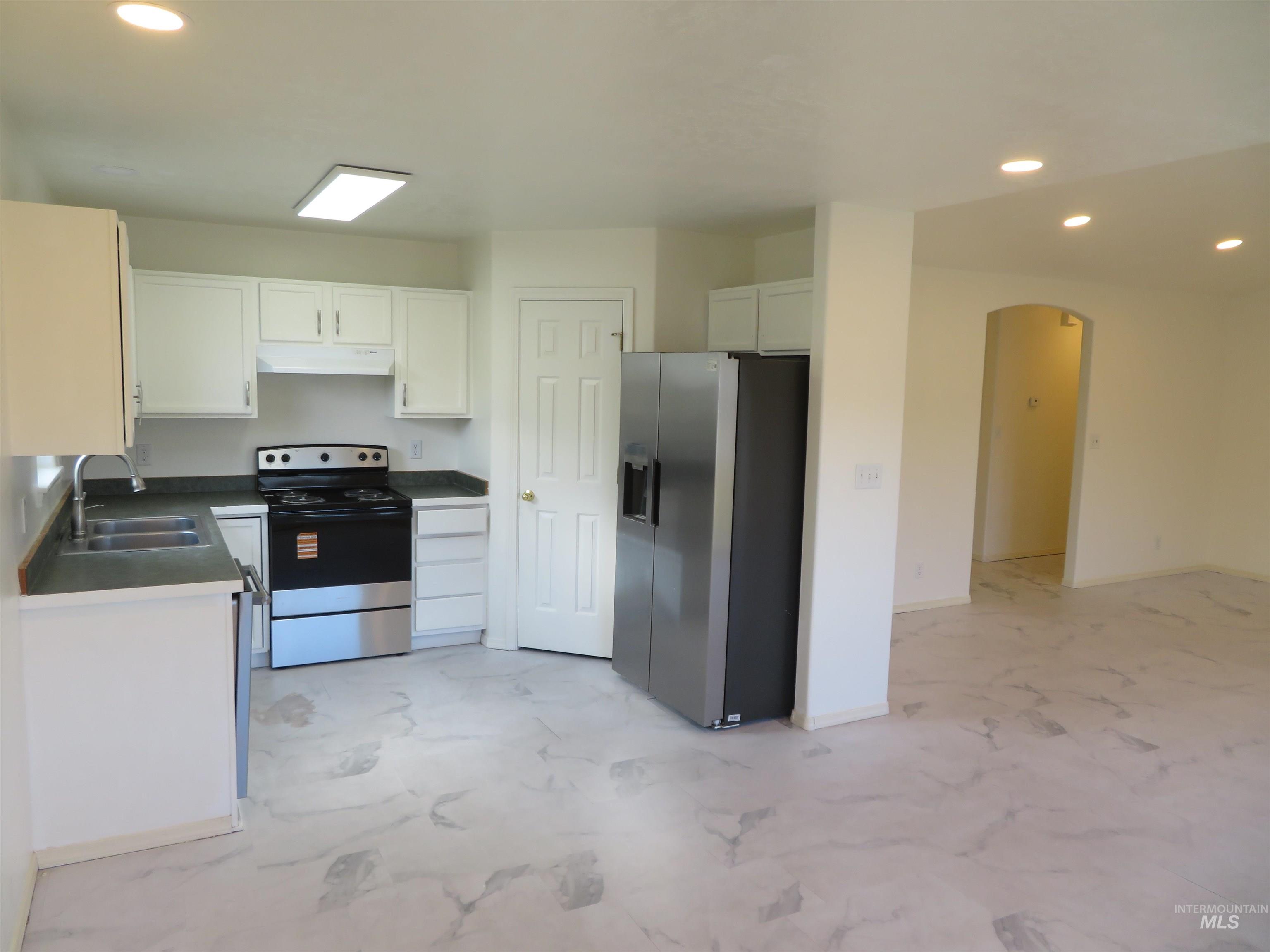 Kitchen featuring recessed lighting, stainless steel appliances, arched walkways, white cabinetry, and under cabinet range hood