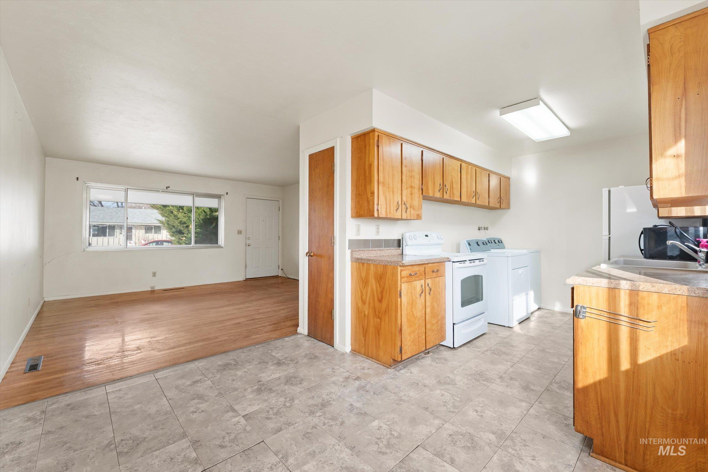 Kitchen with white range with electric cooktop, light countertops, brown cabinets, washer / clothes dryer, and light wood-type flooring