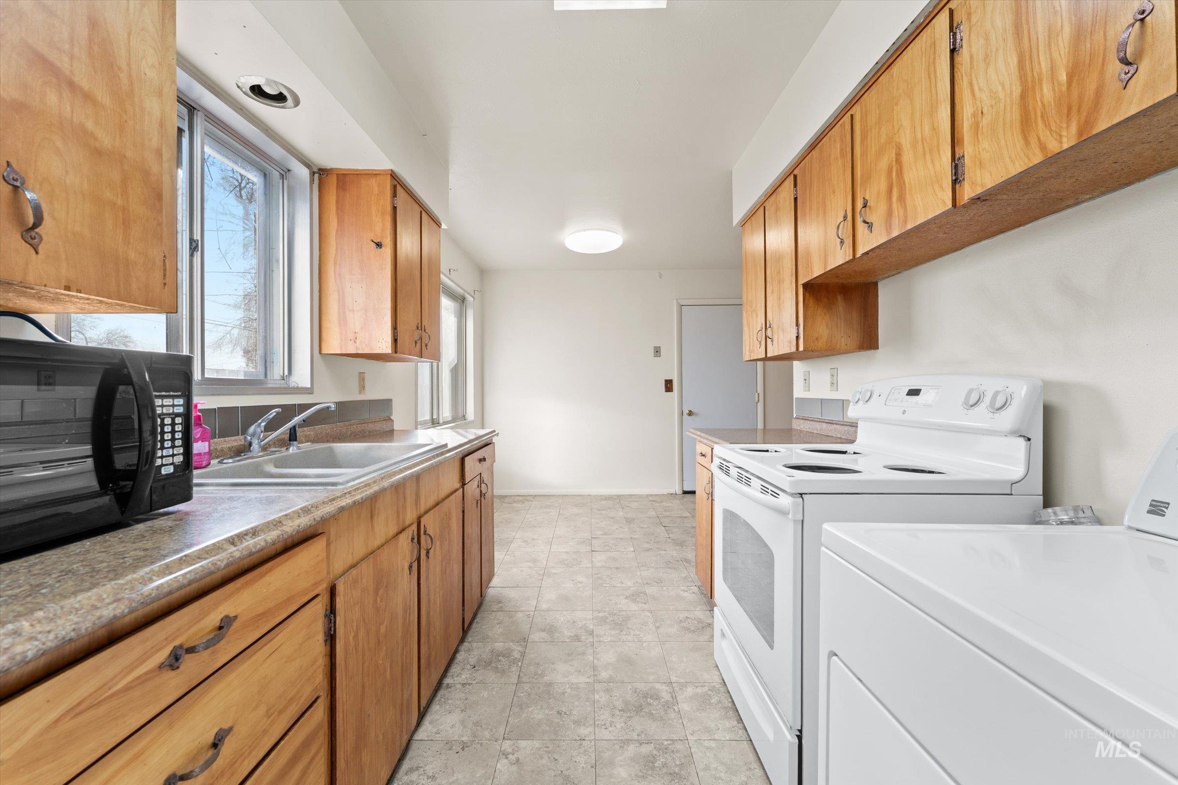Kitchen featuring washer / clothes dryer, brown cabinetry, black microwave, light countertops, and white range with electric cooktop