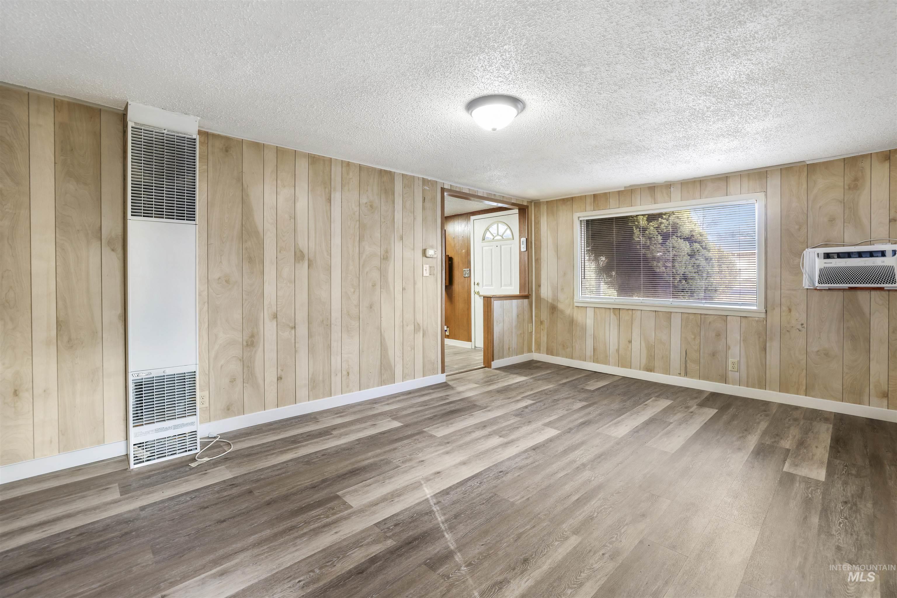 Empty room featuring wood walls, wood finished floors, a textured ceiling, a heating unit, and an AC wall unit
