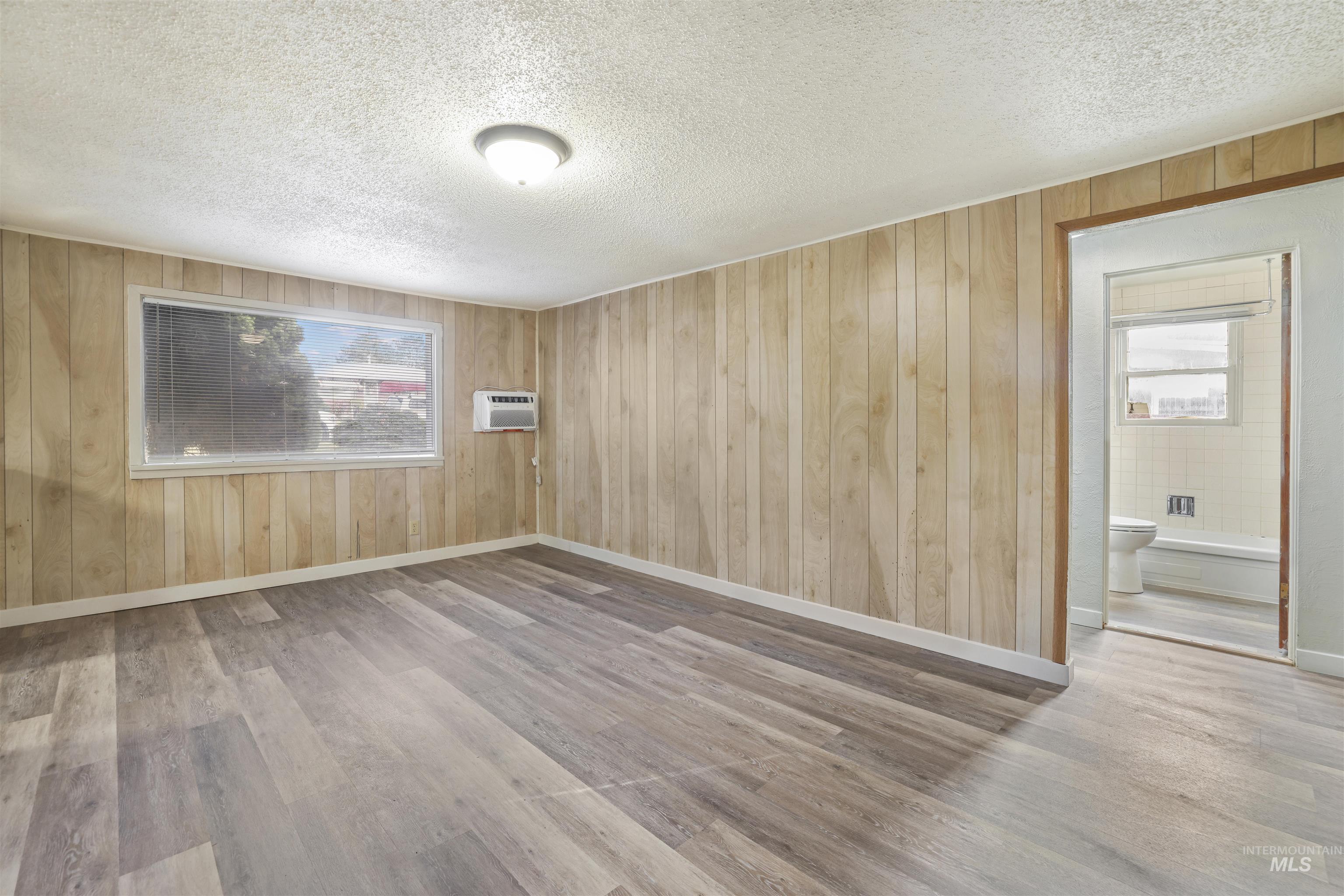 Spare room with wooden walls, light wood-style floors, plenty of natural light, and a textured ceiling