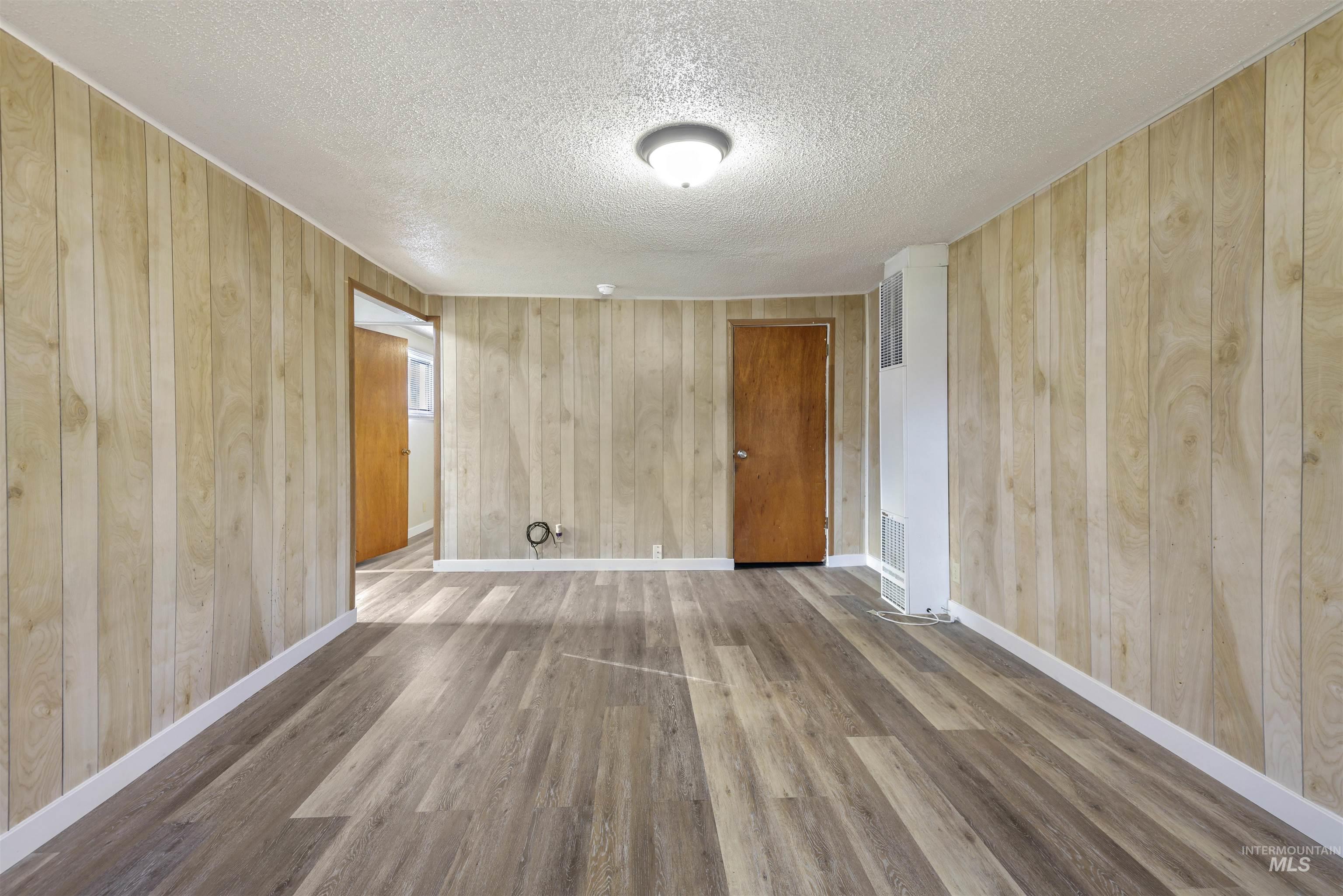 Spare room with wooden walls, a heating unit, wood finished floors, and a textured ceiling