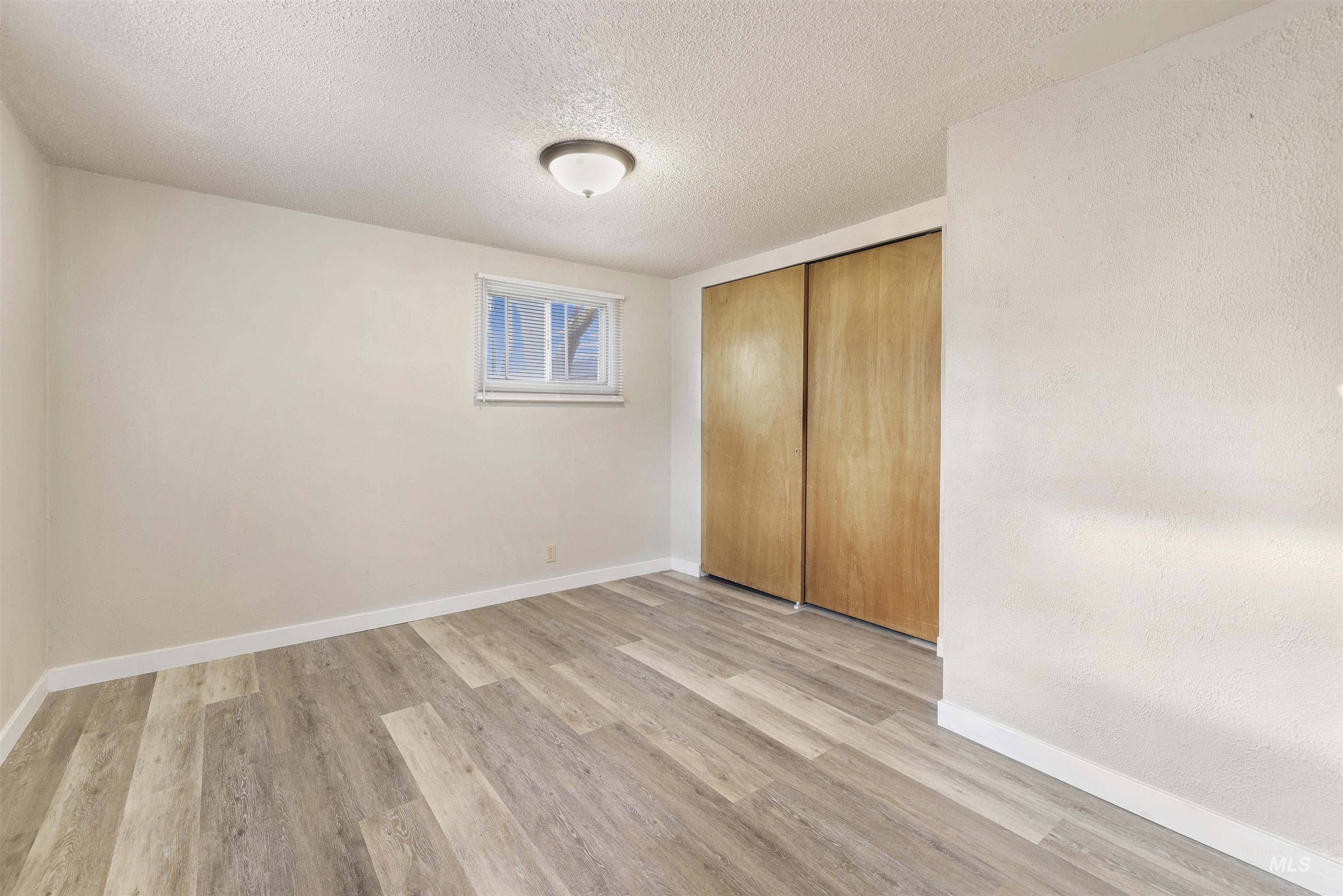 Unfurnished bedroom featuring a textured ceiling, light wood finished floors, and a closet