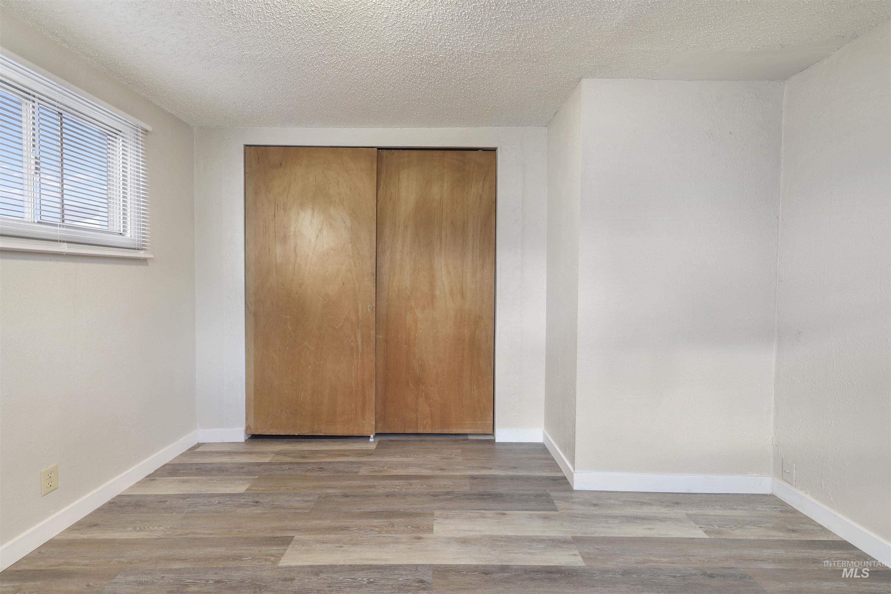 Unfurnished bedroom with a textured ceiling, wood finished floors, and a closet