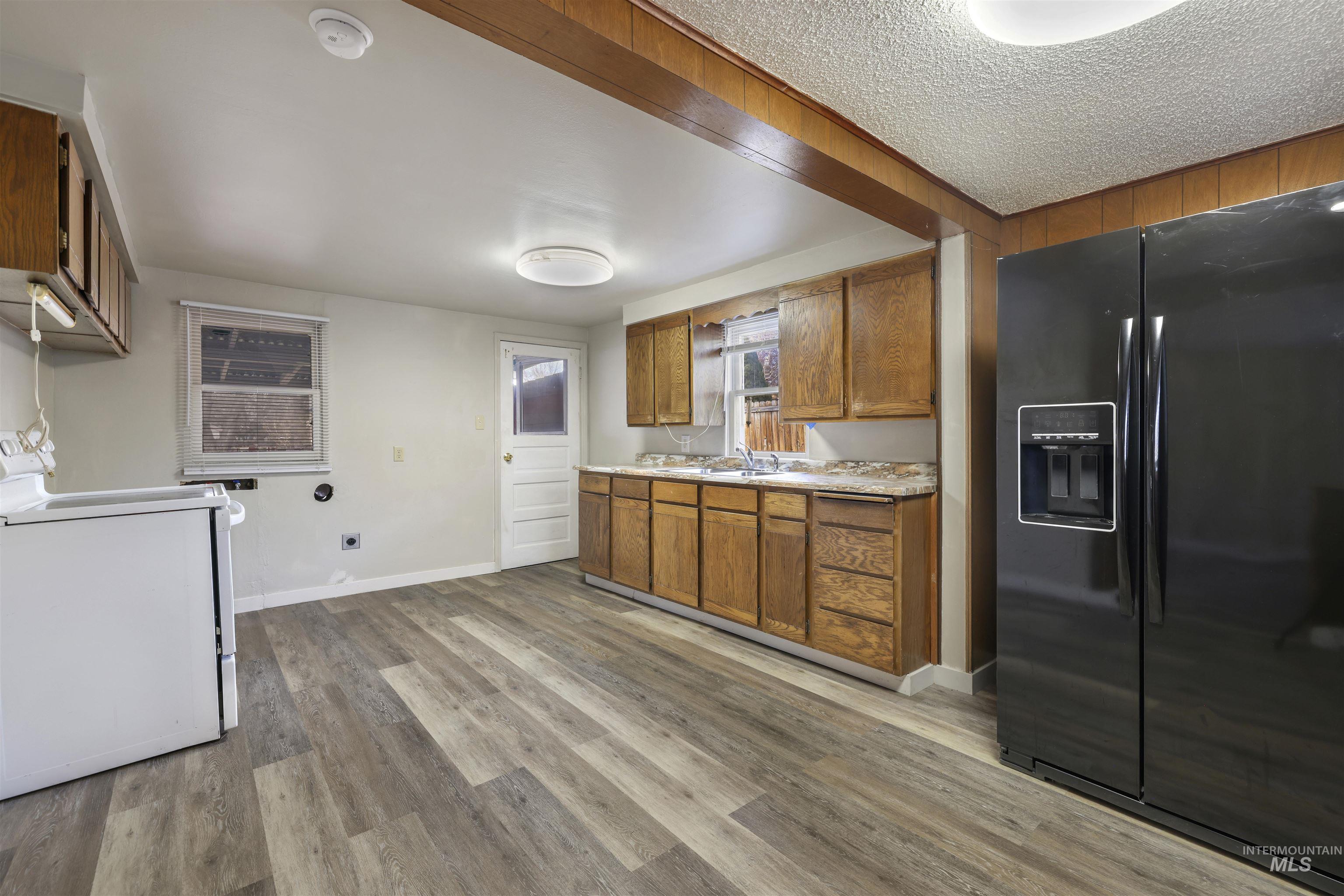 Kitchen with black refrigerator with ice dispenser, brown cabinetry, light countertops, washer / clothes dryer, and light wood-type flooring