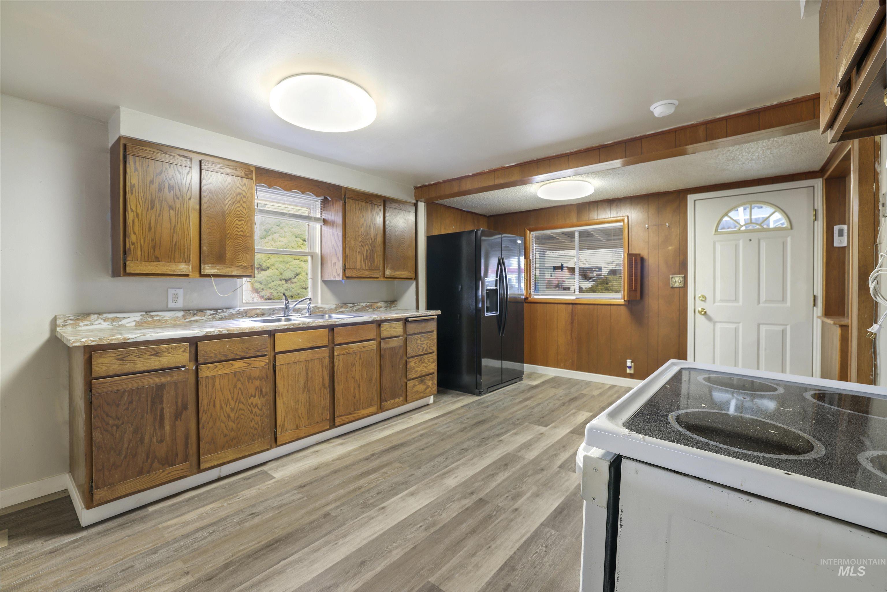 Kitchen with white electric range, black refrigerator with ice dispenser, brown cabinetry, light countertops, and light wood-type flooring